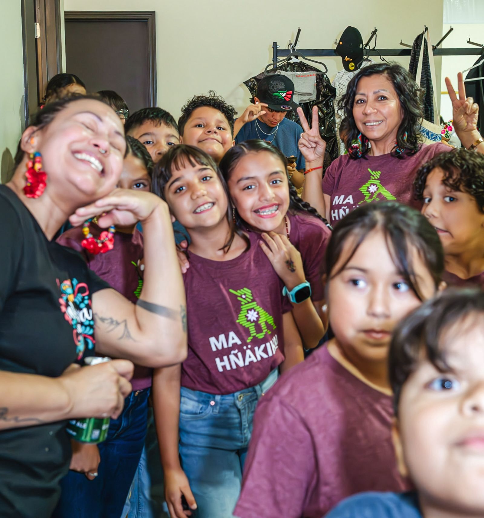 A group of mainly children and two adults in Ma Hnakihu t-shirts smile in a group
