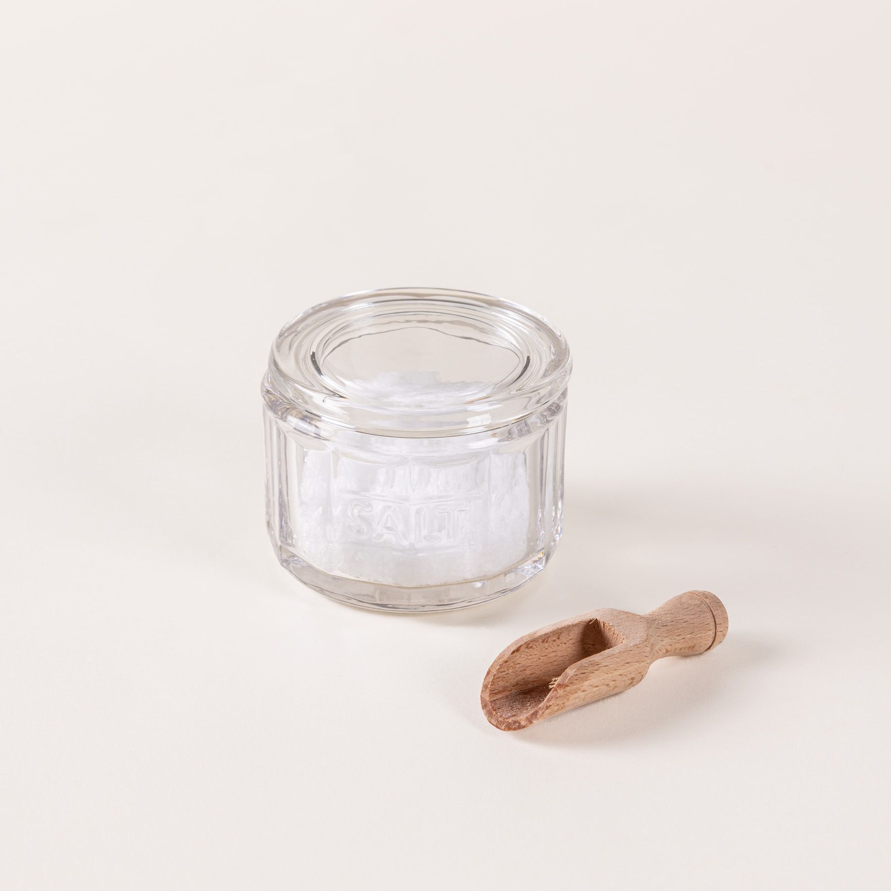 Round glass clear salt canister filled with salt and a small wooden scoop