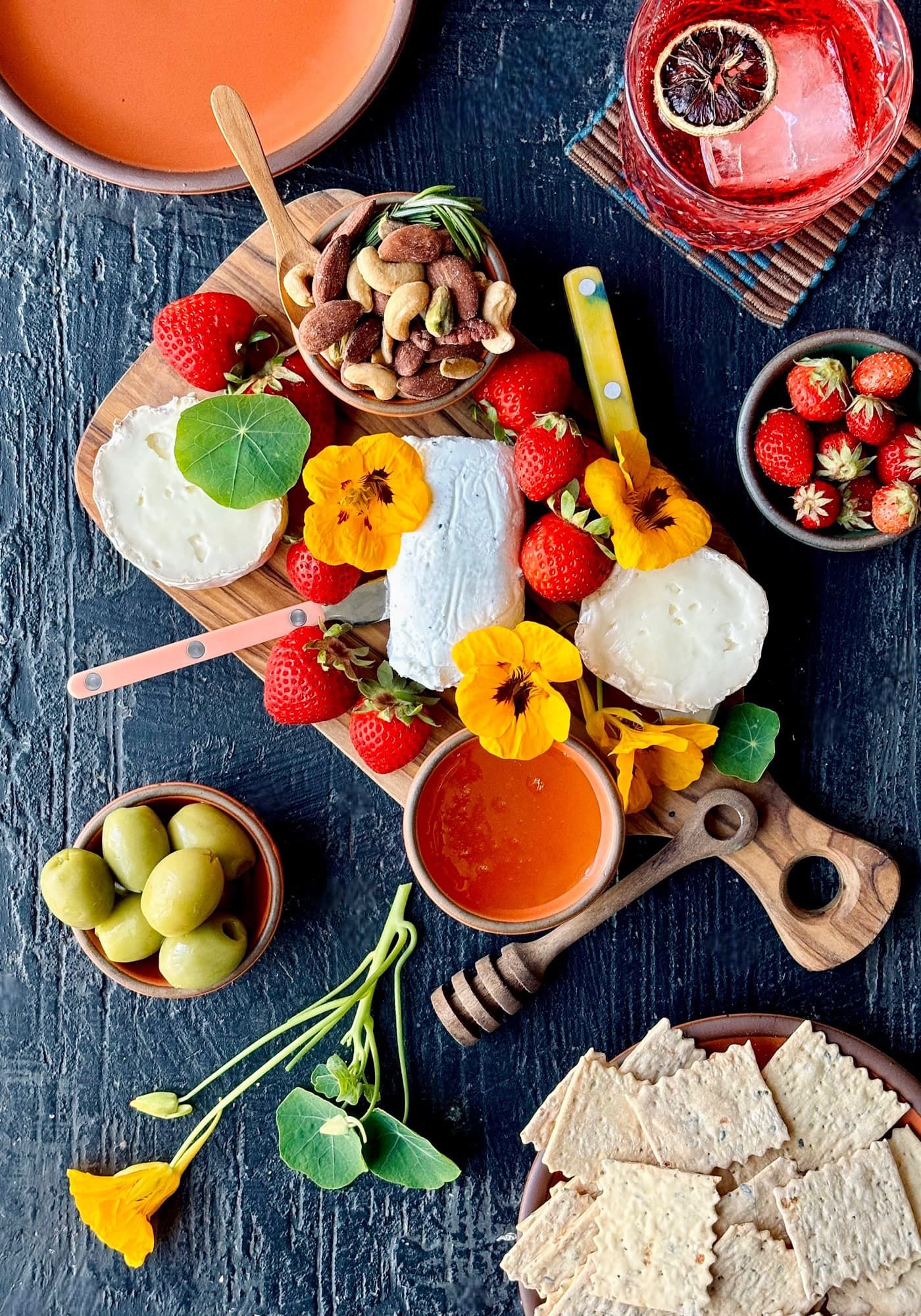 An artful charcuterie board with flowers, olvies, orange plates, and more.