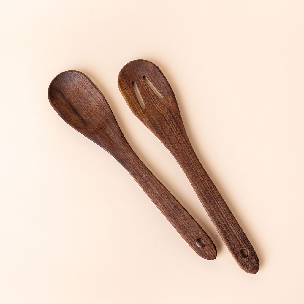 Two large wooden spoons in a deep brown color - one is solid and one has two slots, both have a hole on the end for hanging.