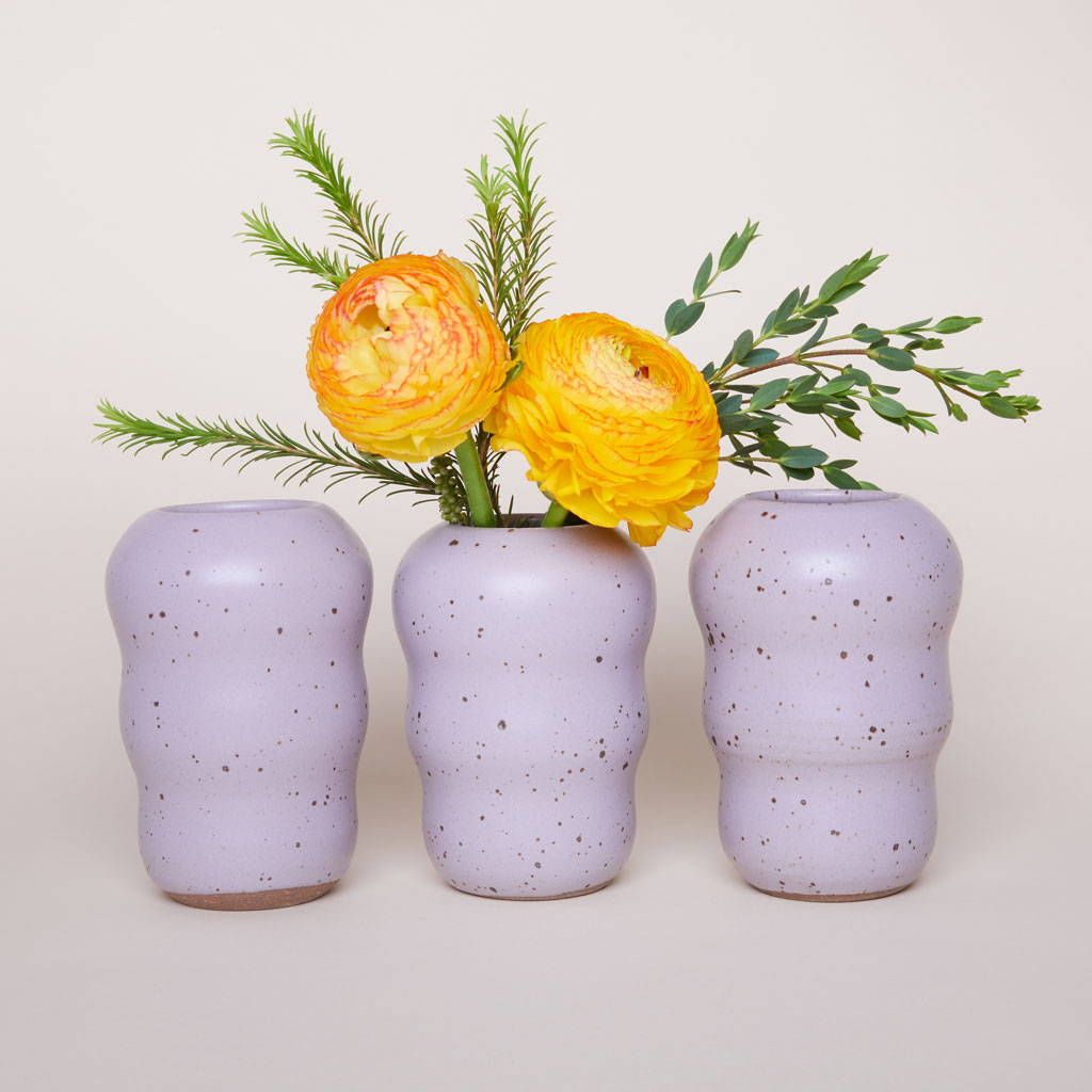 Three curvy ceramic flower vases in a pastel purple with flowers inside the middle one.