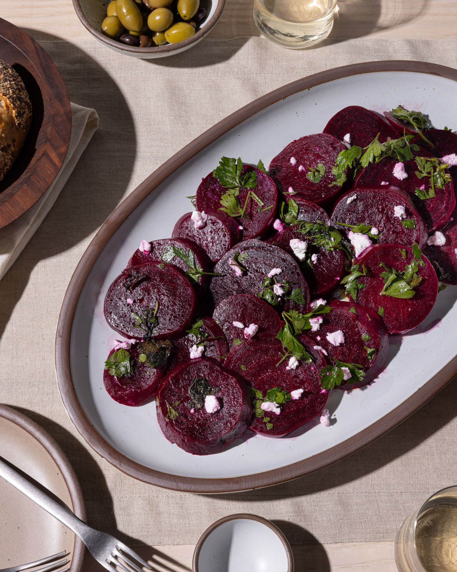 A ceramic white oval platter on a table filled with sliced beets and garnish.