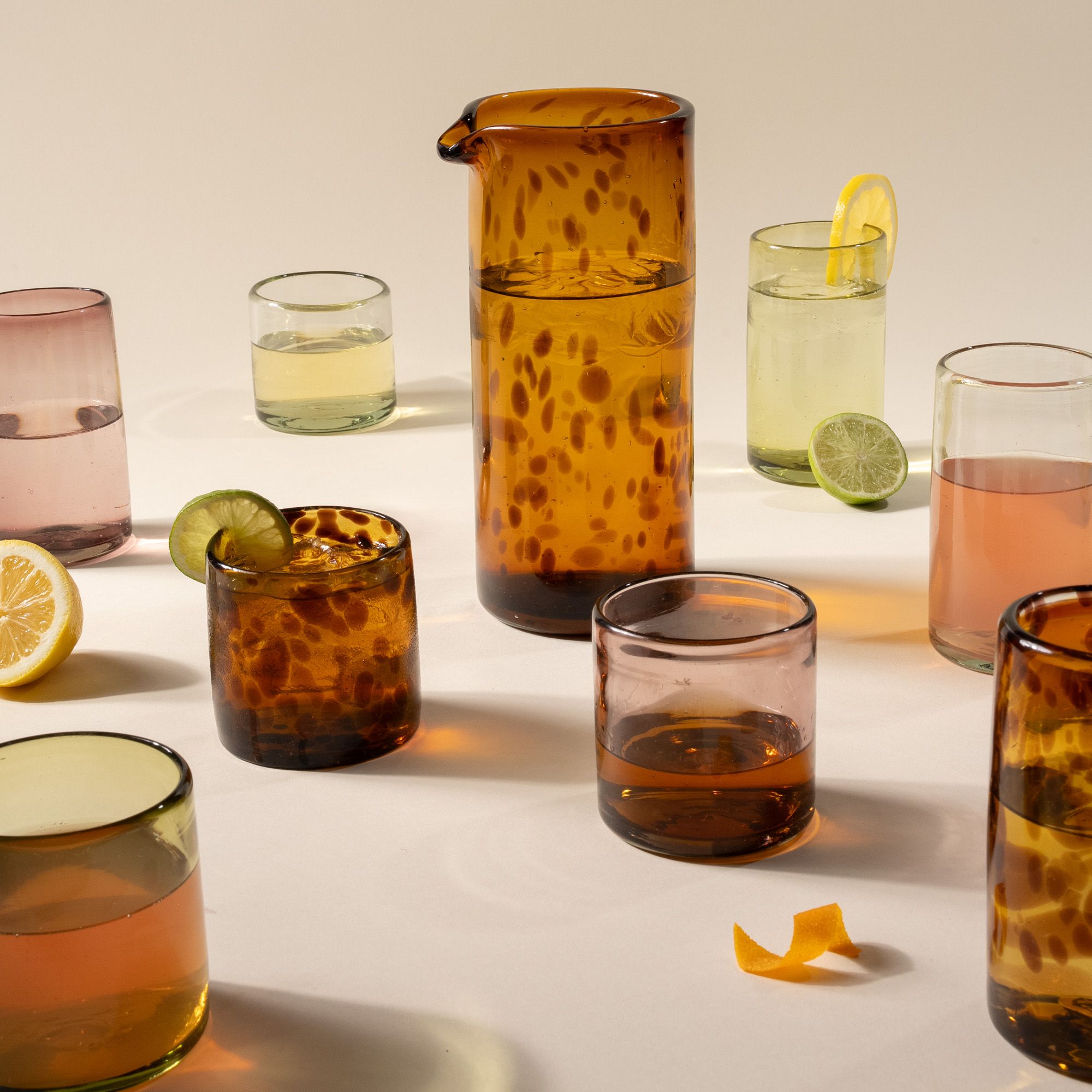 Drinking glasses in different sizes and a pitcher in different colors including tortoiseshell, olive green, soft purple, and clear.