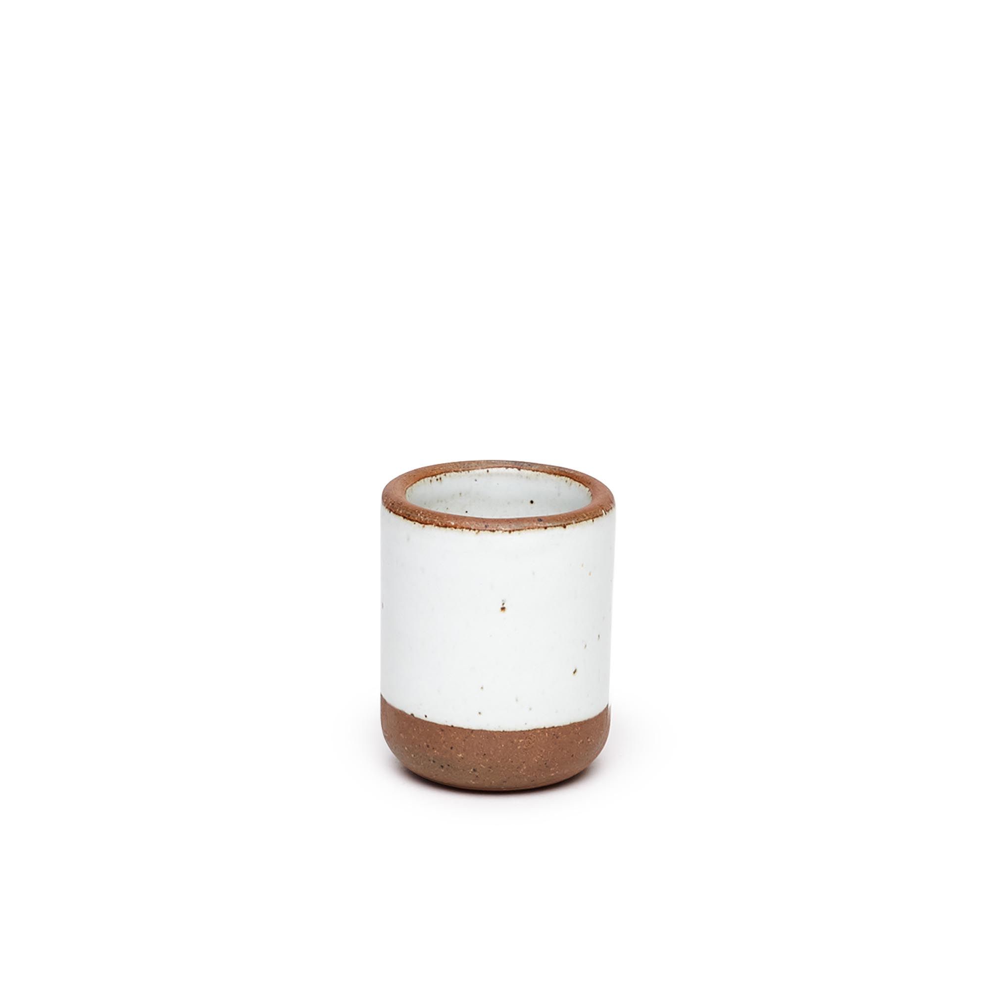 A small, short ceramic mug cup in a cool white color featuring iron speckles and unglazed rim and bottom base.