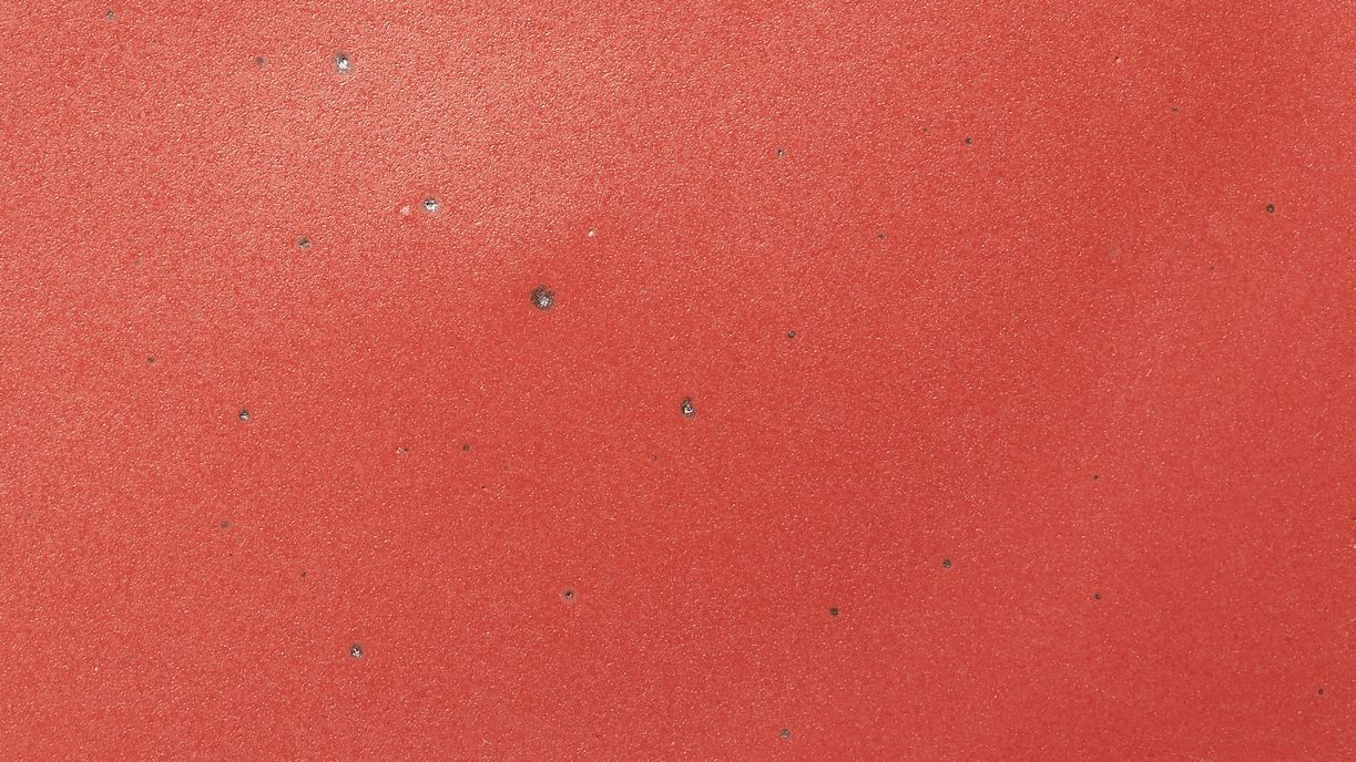 A closeup of a ceramic plate in a bold red color featuring iron speckles