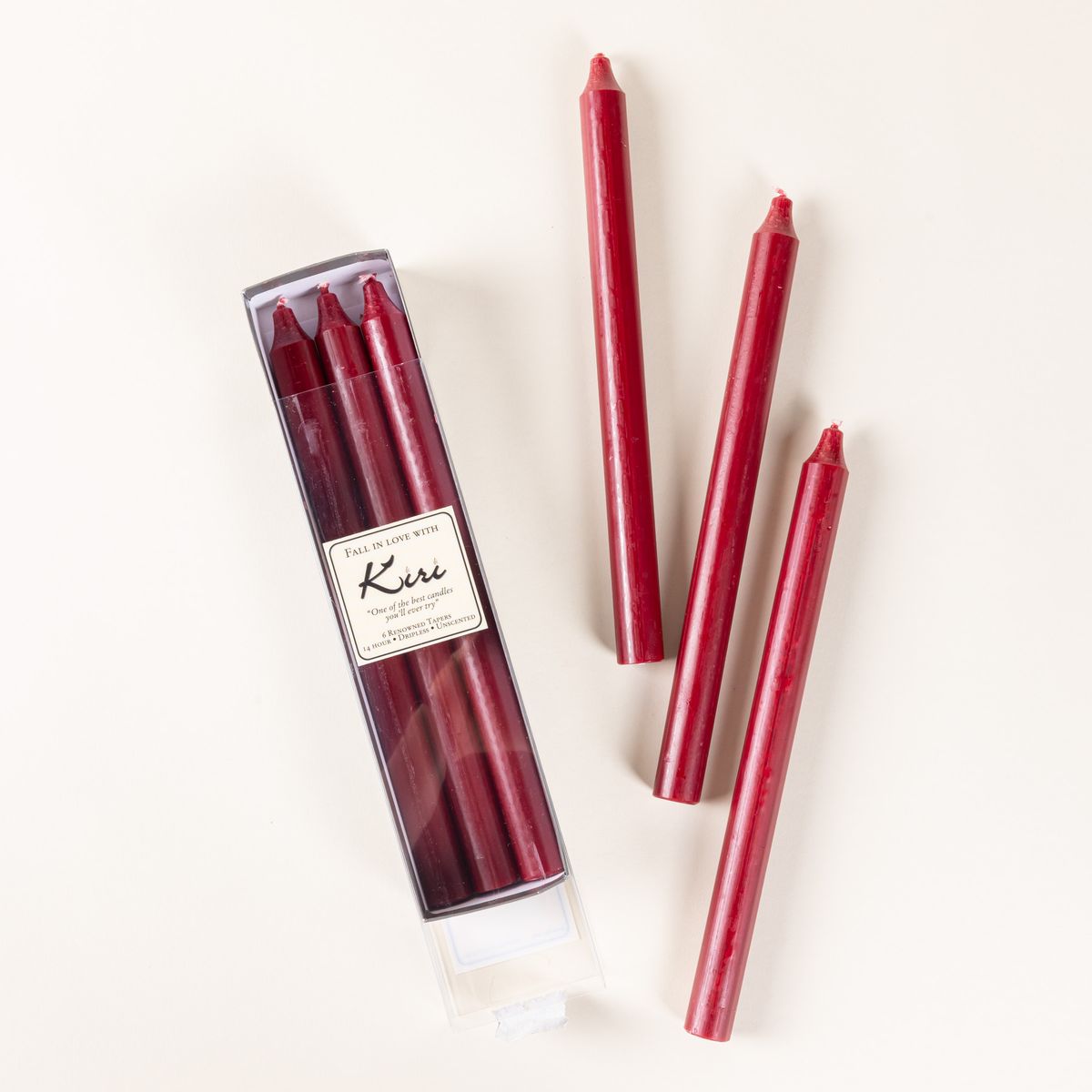 A narrow box of dark red taper candles, with 3 arranged outside of the box.