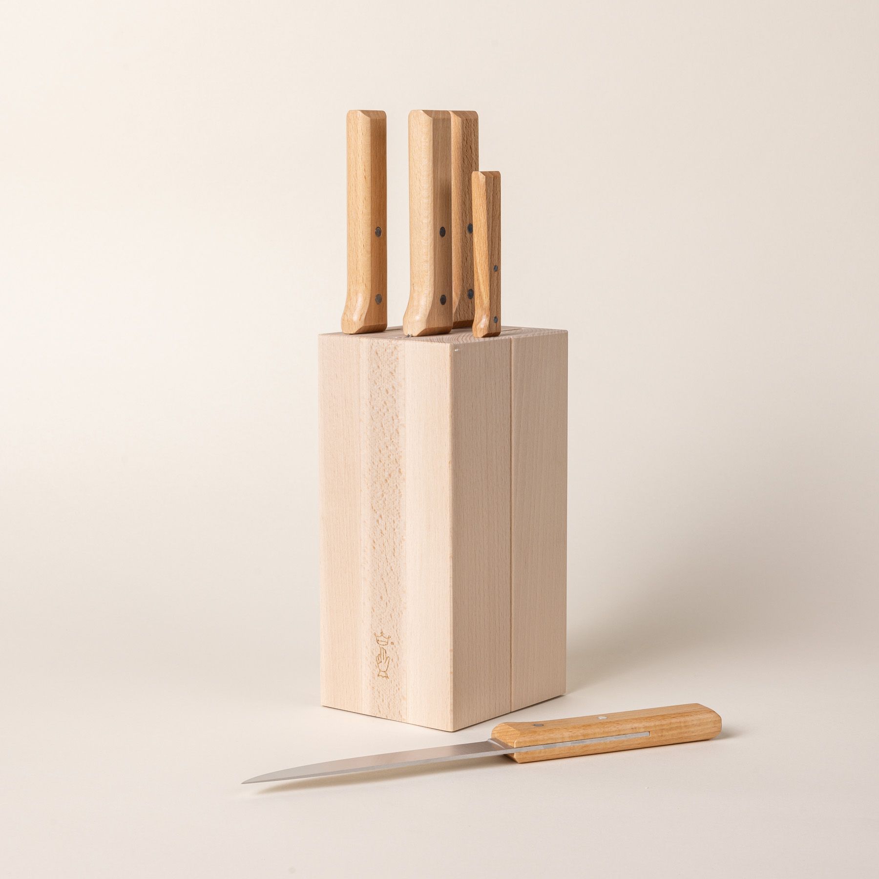 A tall rectangular wooden block with knives inside and the wooden handles sticking out at the top. One knife is laying flat next to the block.