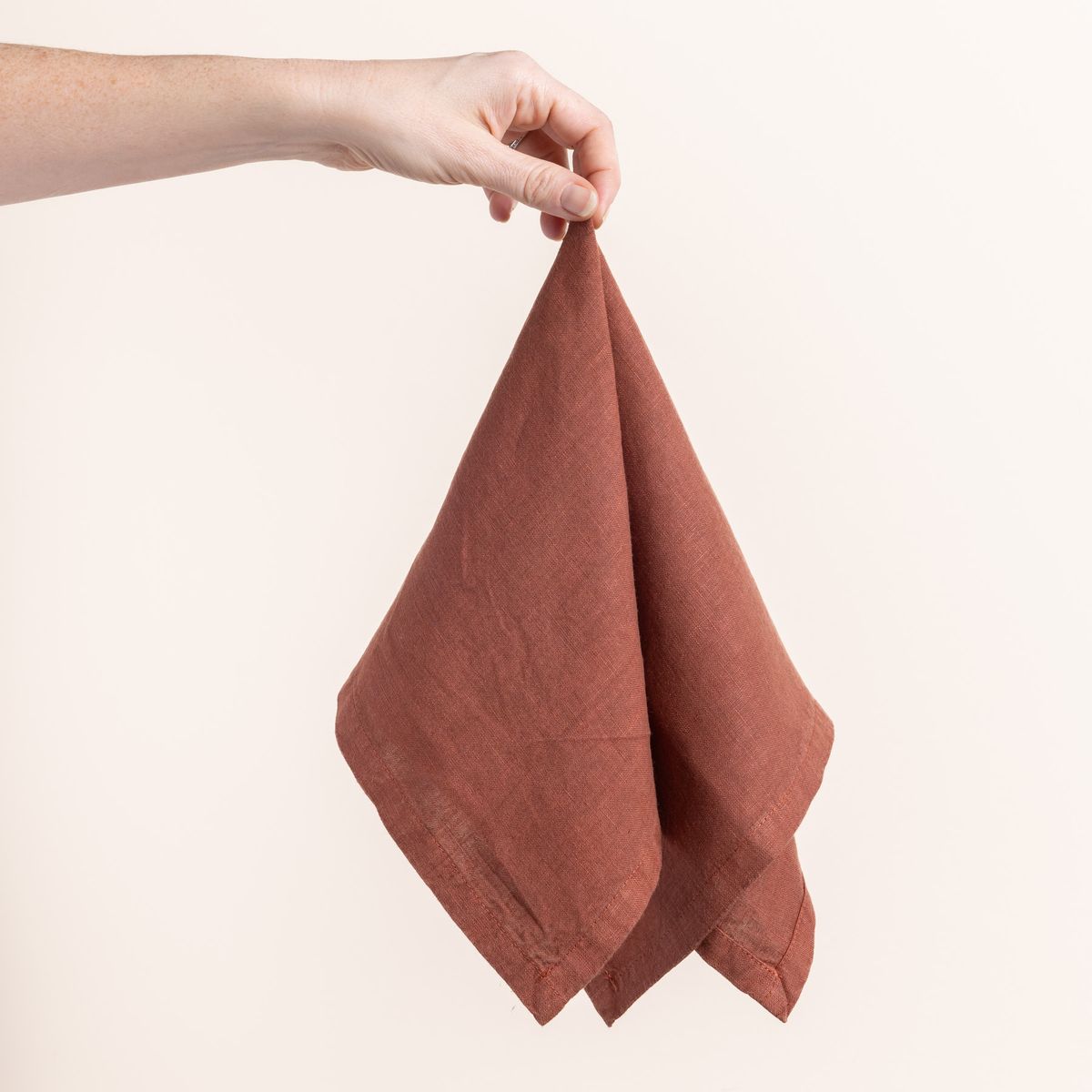 Hand holding a linen napkin in an terracotta color from the center 