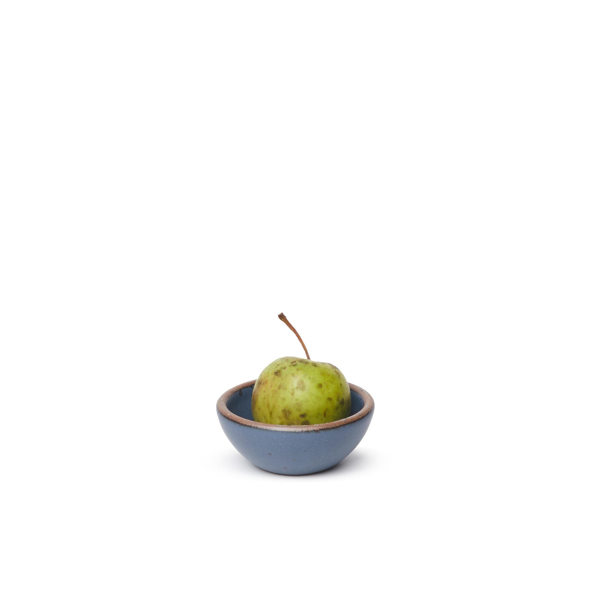 A tiny rounded ceramic bowl in a toned-down navy color featuring iron speckles and an unglazed rim, with a pear inside