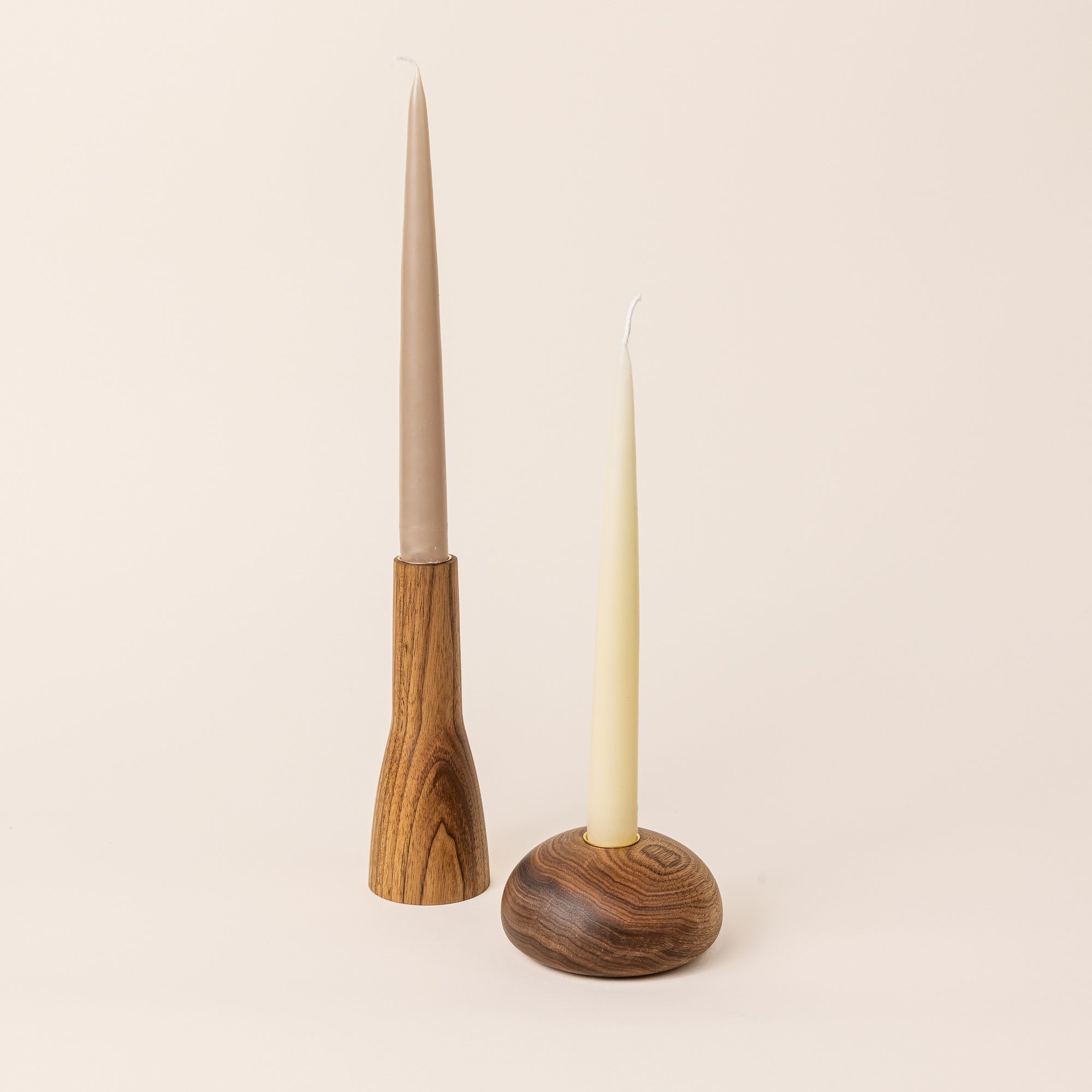 Two butternut wood candle holders, one is a more narrow organic shape, and the other is shaped more like a dome. Taper candles sit on top of each.