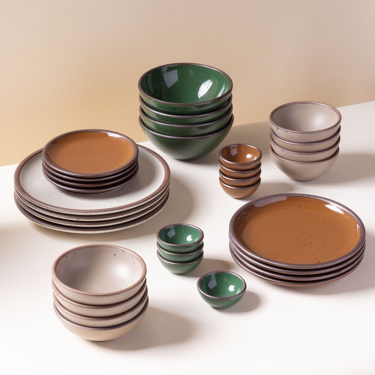 A rustic ceramic dinnerware set with stacked plates, bowls, and dipping dishes in earthy brown, beige, and green tones.