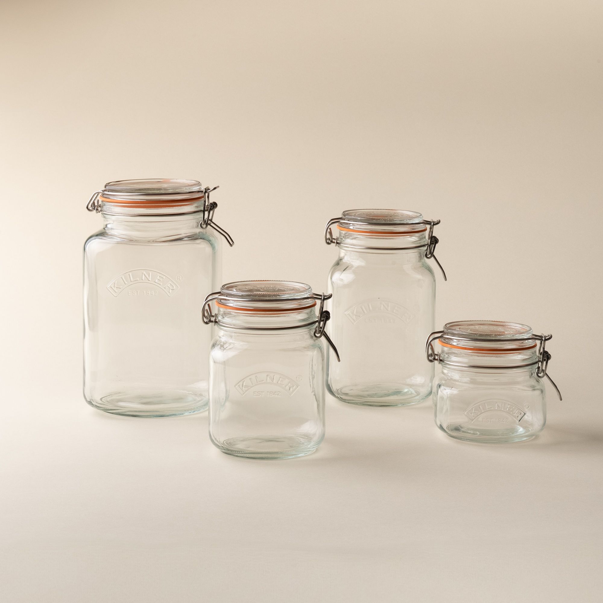 4 storage glass square jars in a row of largest to smallest, each topped with a lid with a rubber seal and steel clip closure.