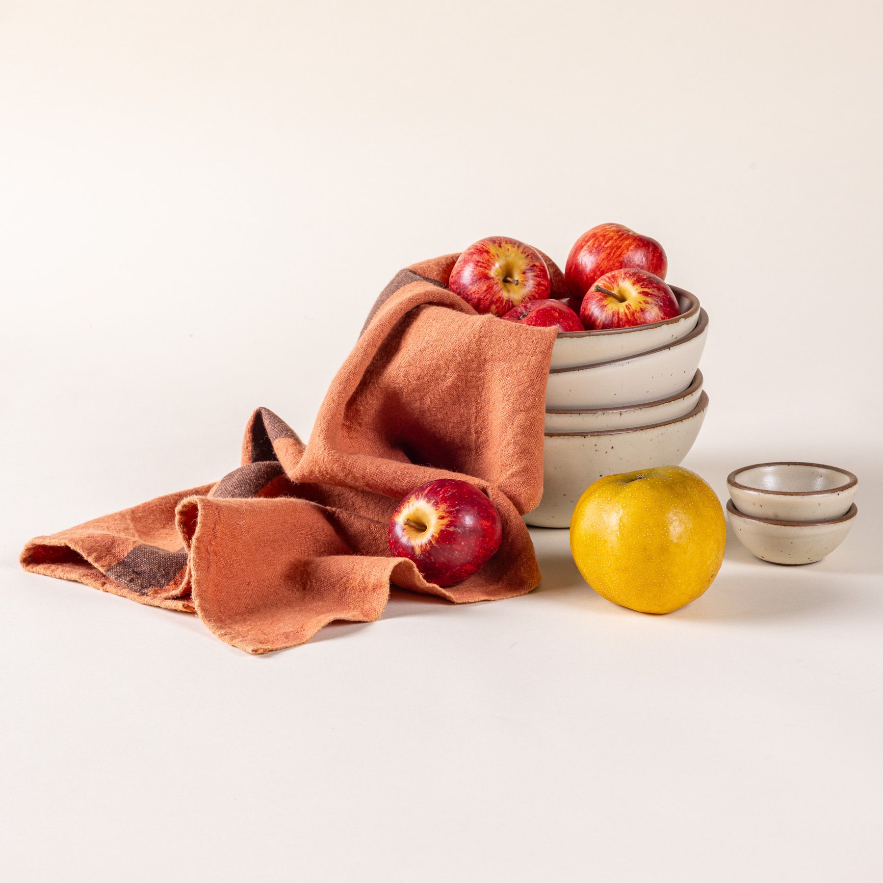 A terracotta linen towel with a stack of cream ceramic bowls with apples