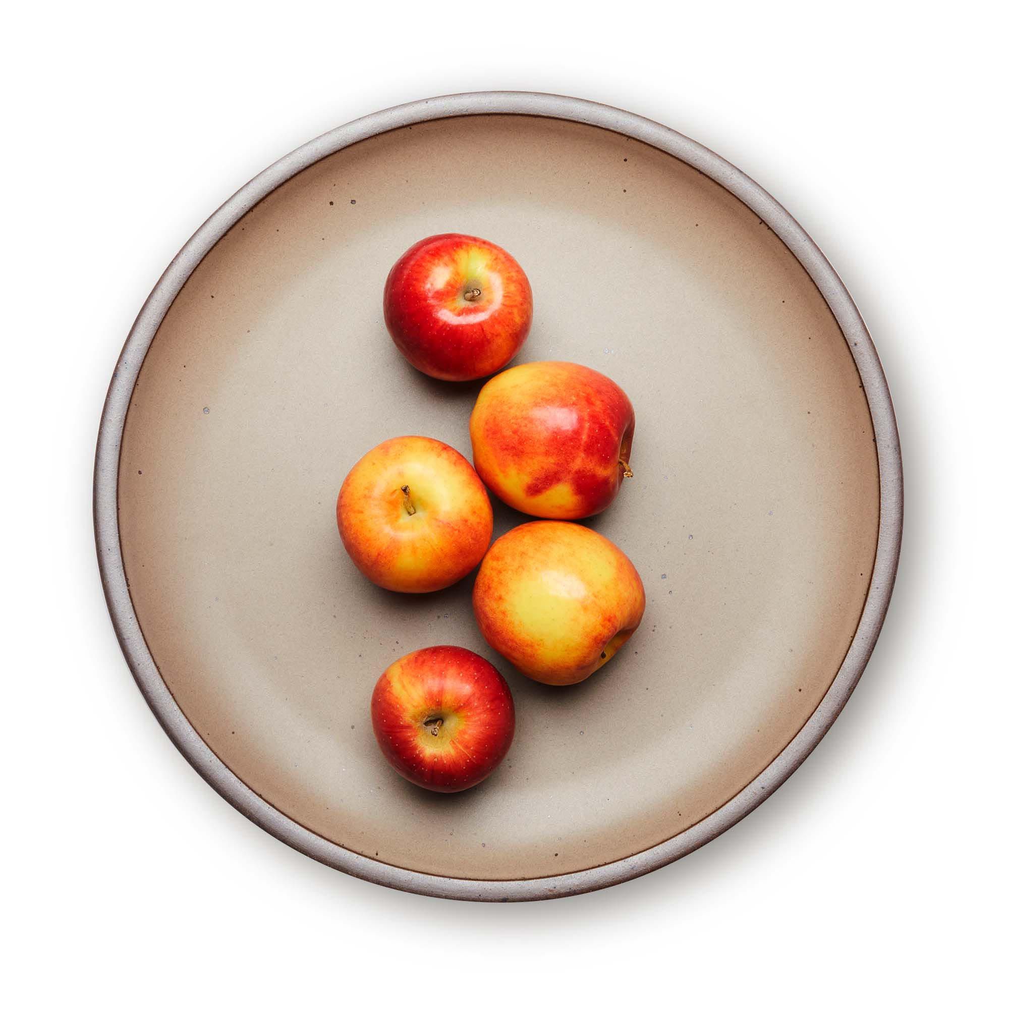 Apples on a large ceramic platter in a warm pale brown color featuring iron speckles and an unglazed rim.