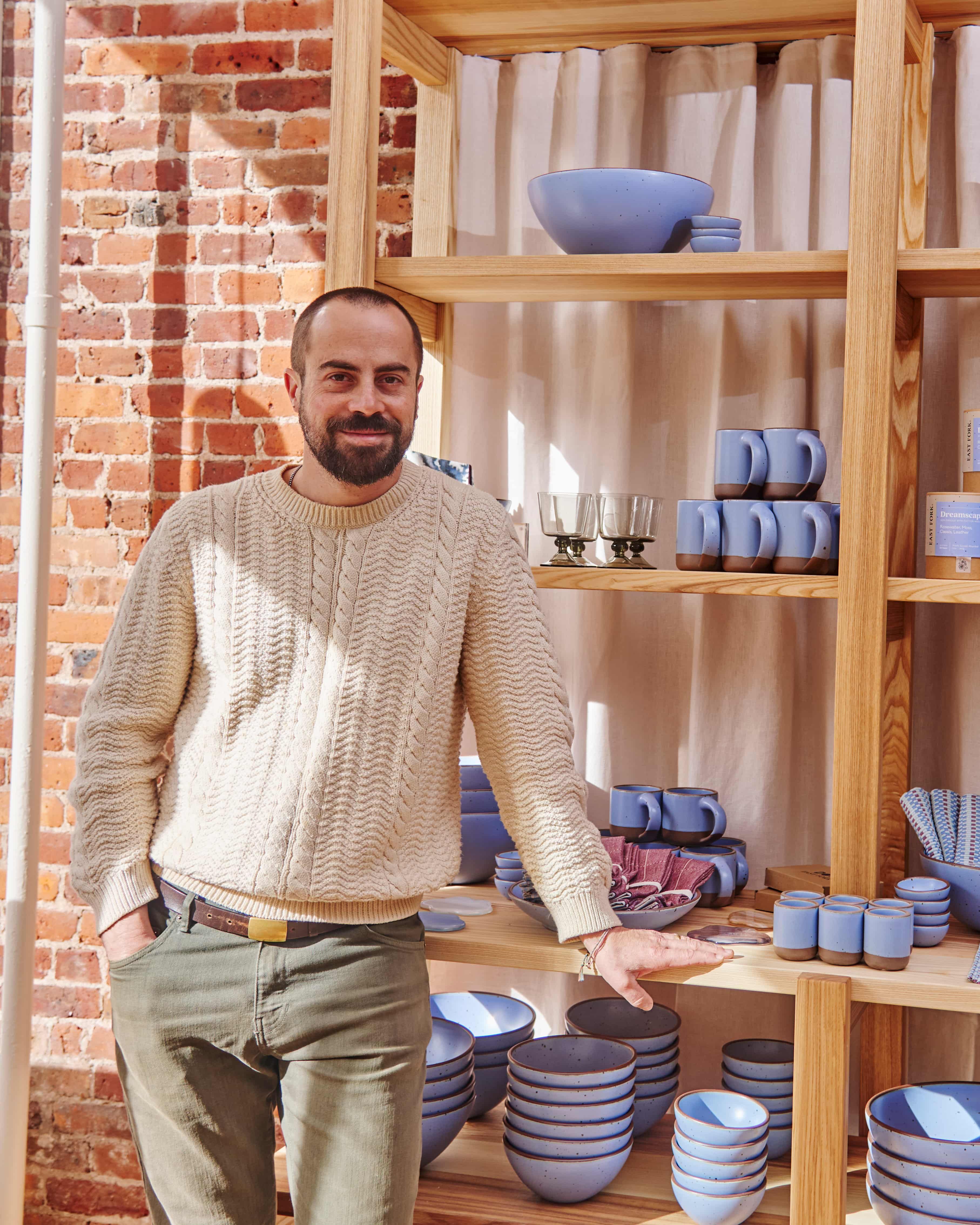 Alex standing in East Fork Brooklyn in front of a shelf of periwinkle mugs, bowls, and plates