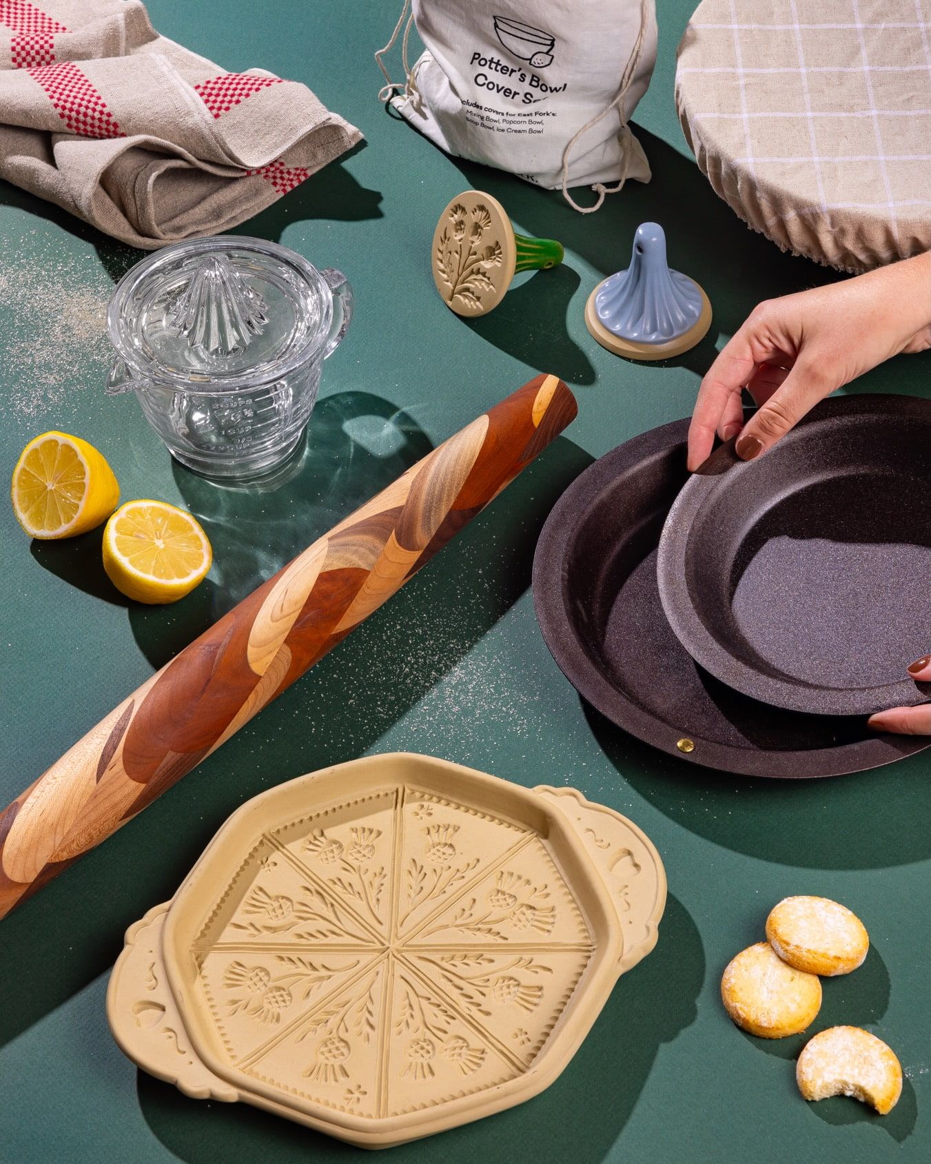 An artful display of baking tools and accessories with a hand reaching for an iron pie plate against a green background.