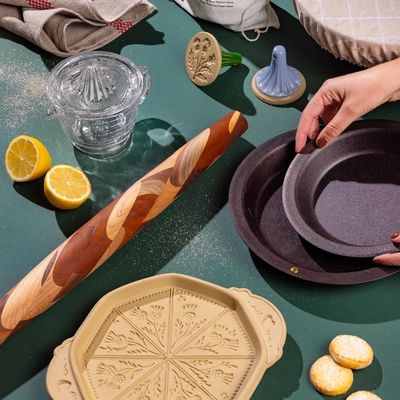 An artful display of baking tools and accessories with a hand reaching for an iron pie plate against a green background.