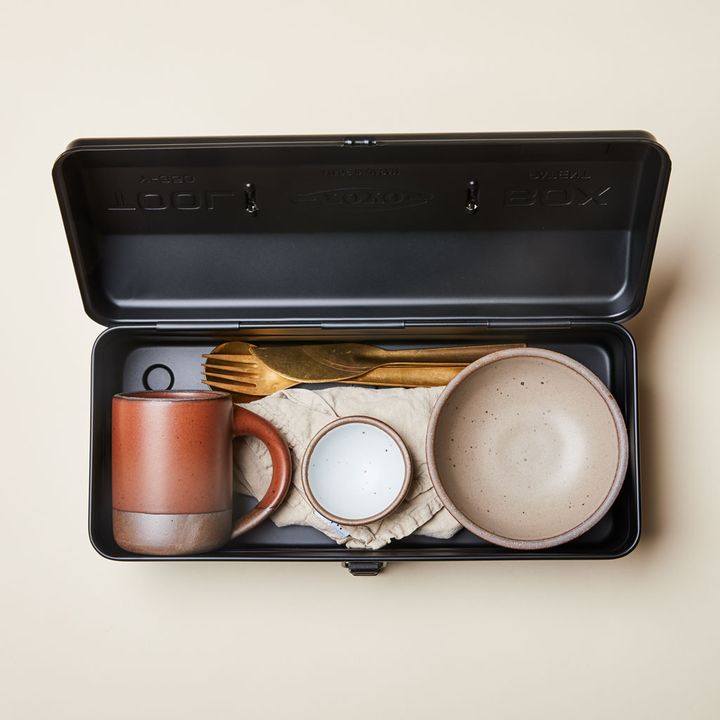 Open black rectangular tin box with The Mug, napkin, Bitty Bowl, Everyday Bowl and cutlery set fitting comfortably inside.