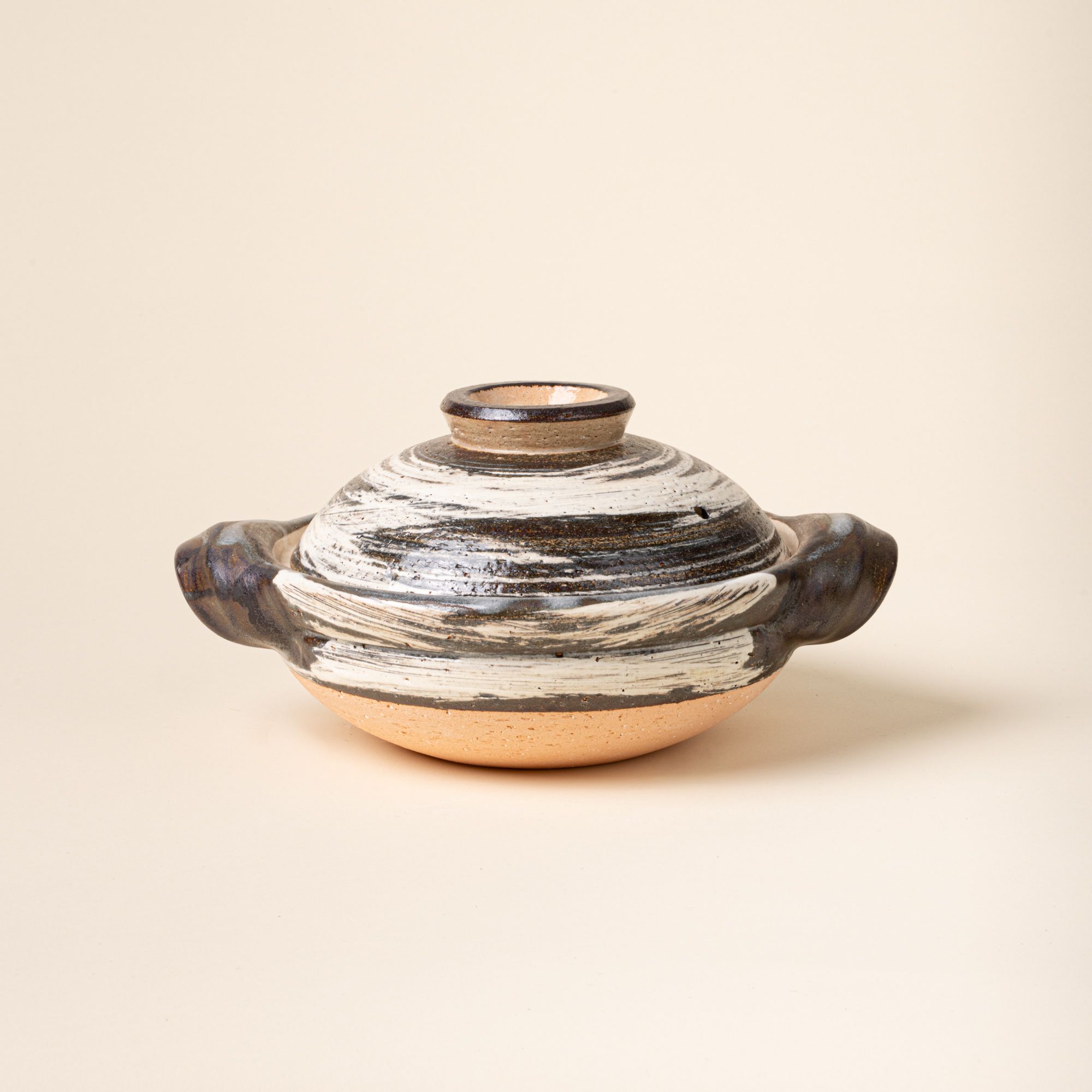 Handcrafted ceramic donabe with side handles and a matching lid, finished in a black-and-white brushed glaze over natural clay.