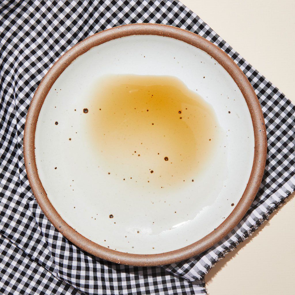 Translucent light brown puddle of sherry vinegar on an East Fork plate in Eggshell on a black and white gingham cloth