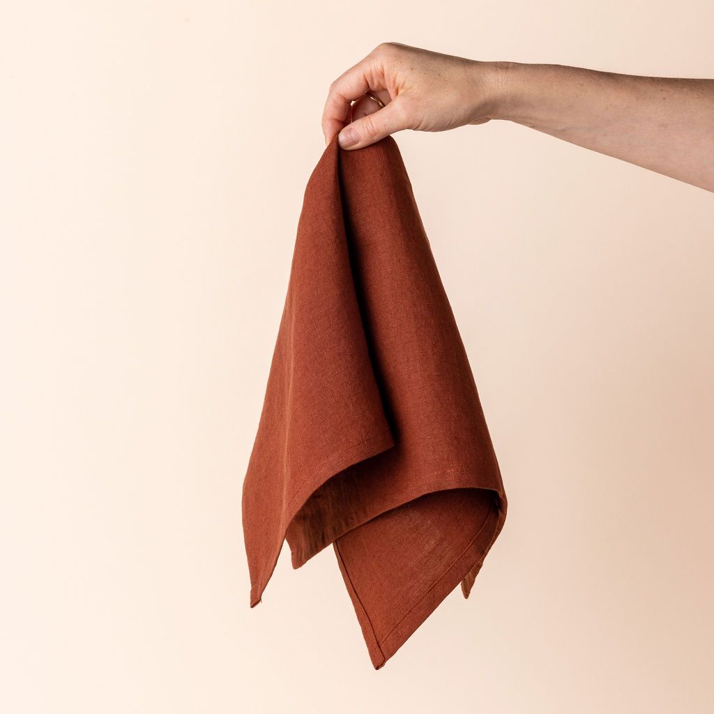 Hand holding a linen napkin in an terracotta color from the center 