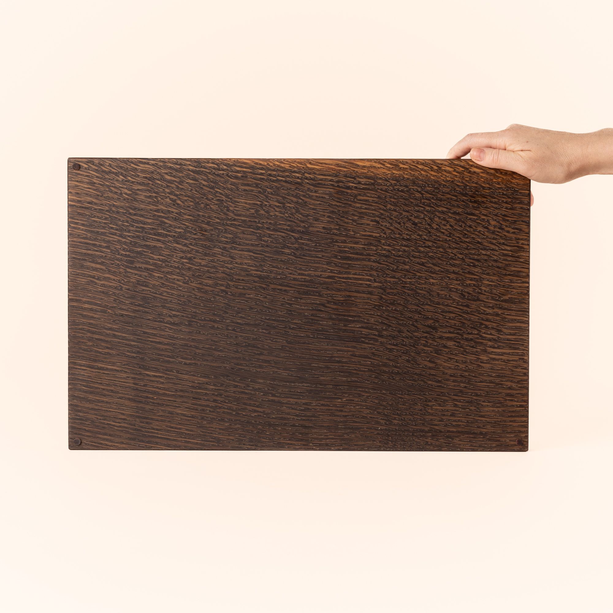 A hand holds up a rectangle of wood that has been finished in an ebonized stain