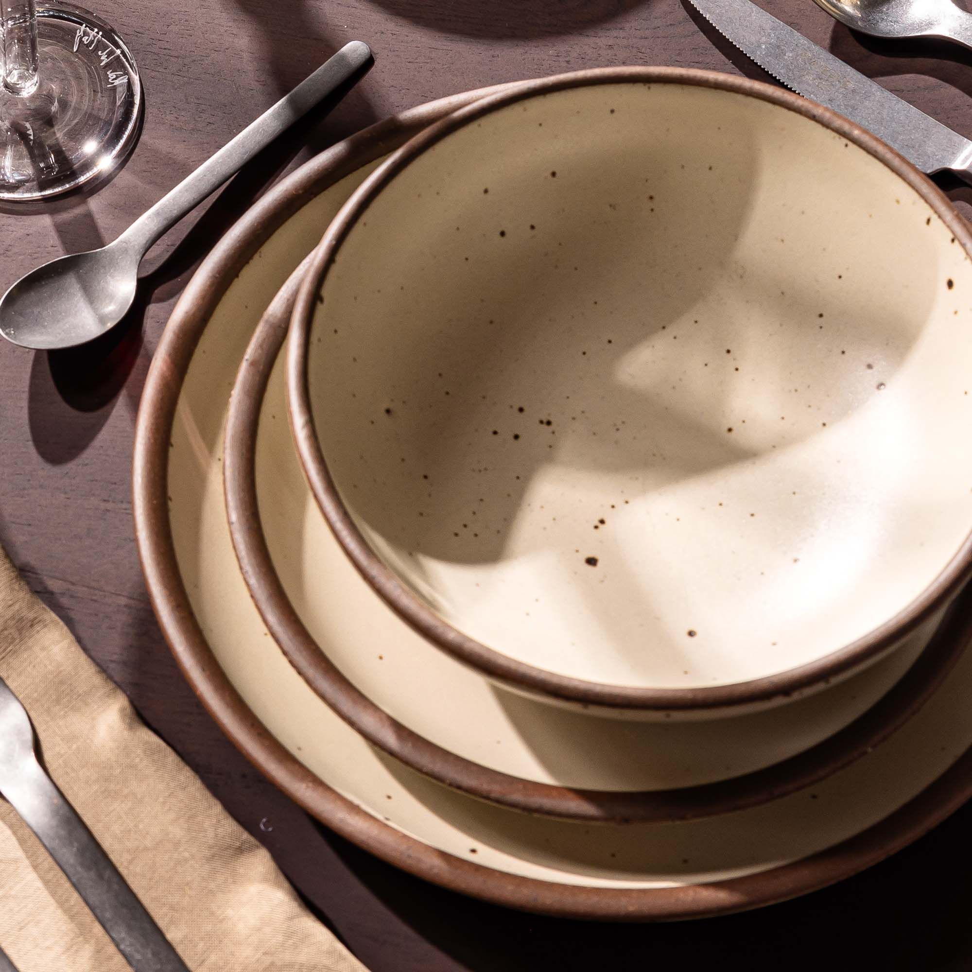 A stacked place setting with a dinner plate, side plate, and shallow dinner bowl in a cream off-white color.