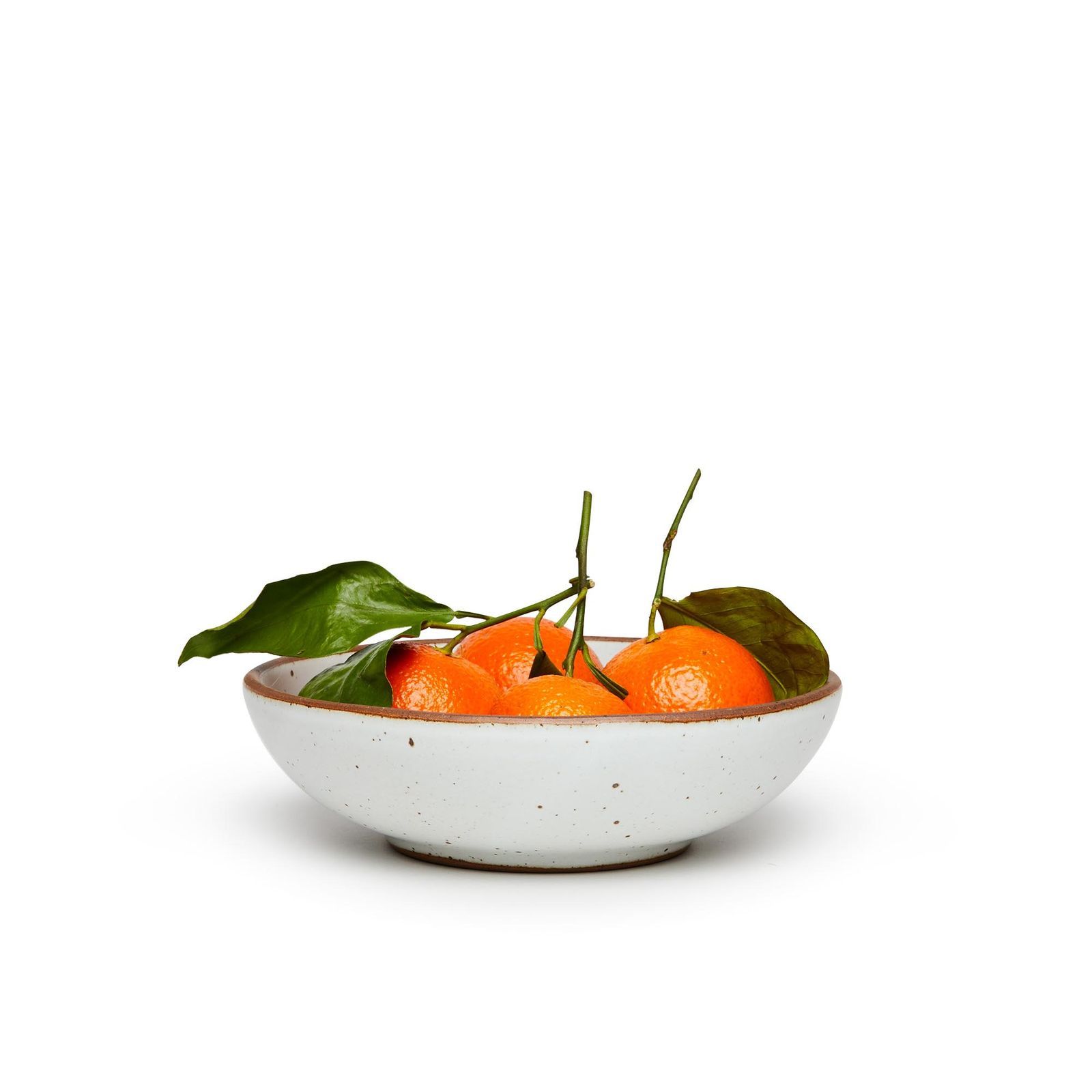 A blueish-white bowl, comfortably holding four small oranges with their leaves and stems still attached.