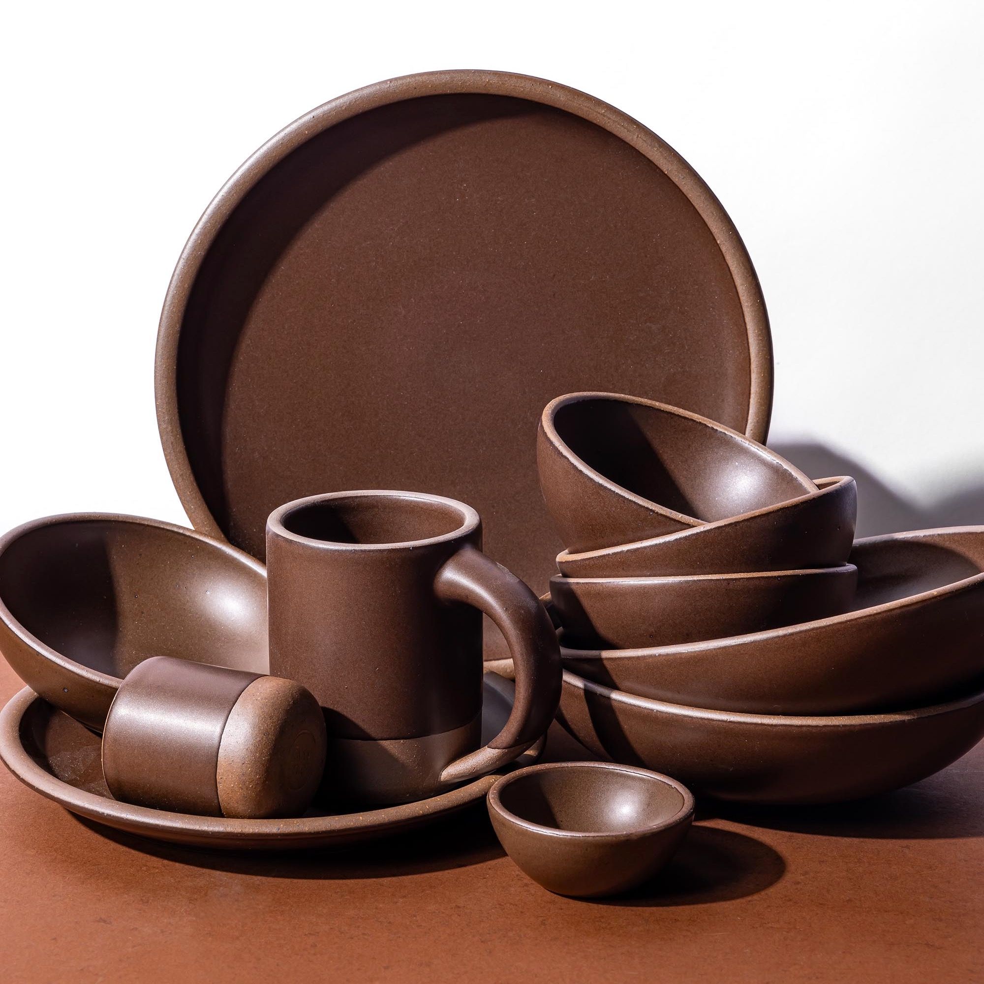 An up close look at ceramic plates, bowls, and cups, in a dark brown color stacked and arranged close together.