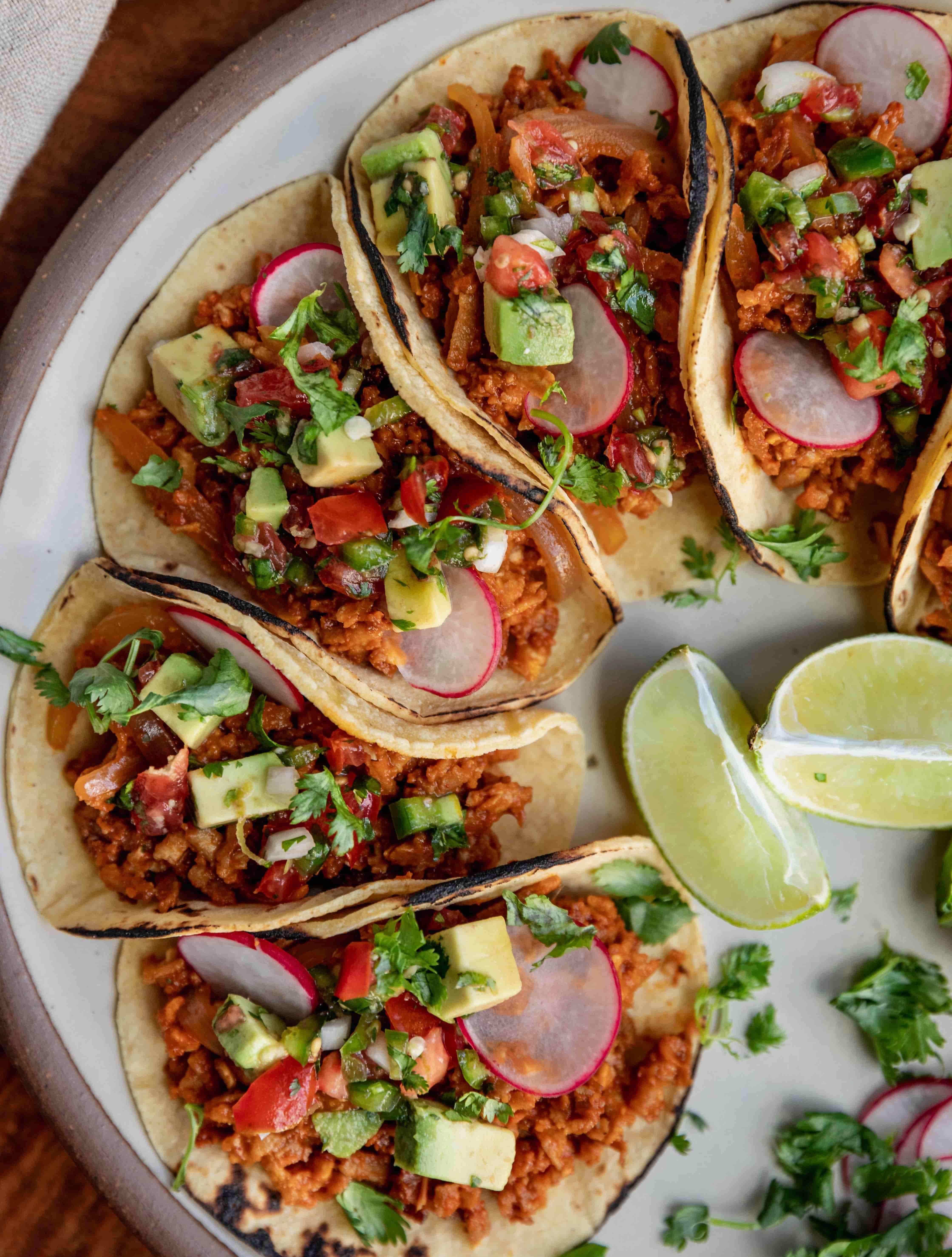 Corn tortilla tacos with cilantro and lime wedges on a ceramic white plate.