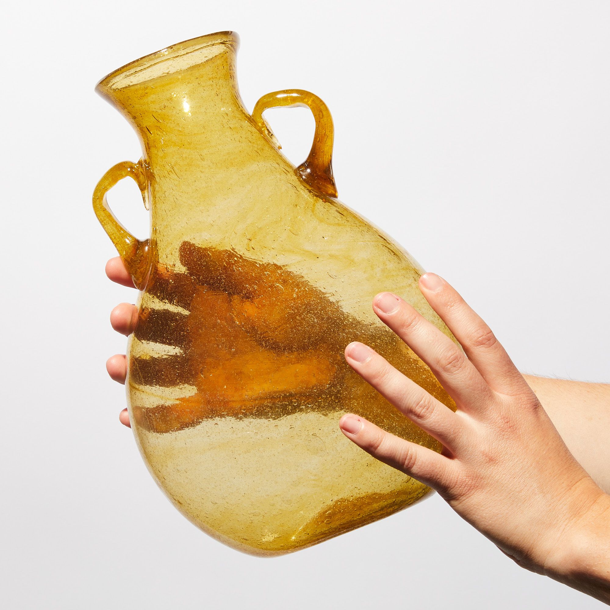 hands holding a translucent yellow vase, narrowing at the top with two small handles