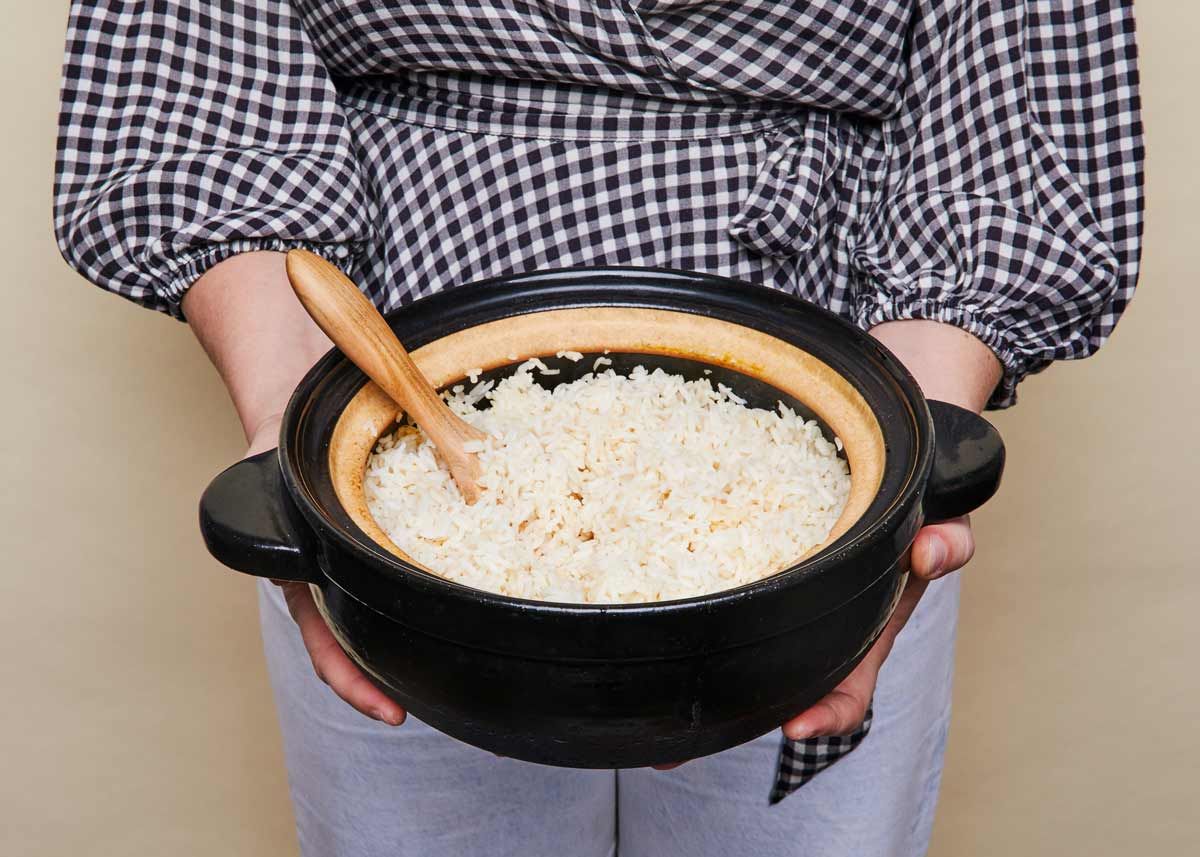 Hands holding a dark clay pot with rice 
