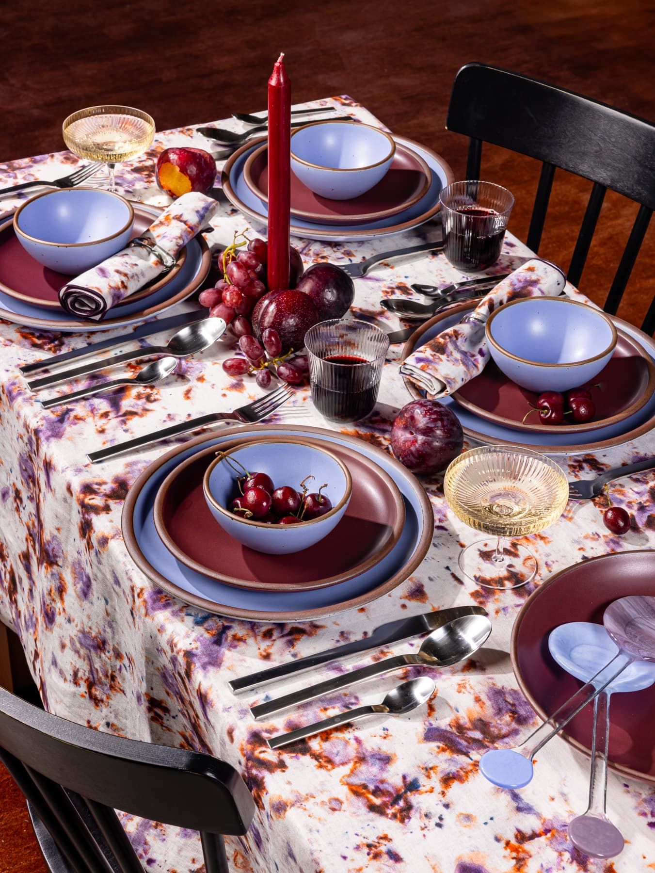 A table filled with ceramic pottery in periwinkle and plum colors, matching marbled tablecloth, silverware, and glasses filled with red wine and champagne