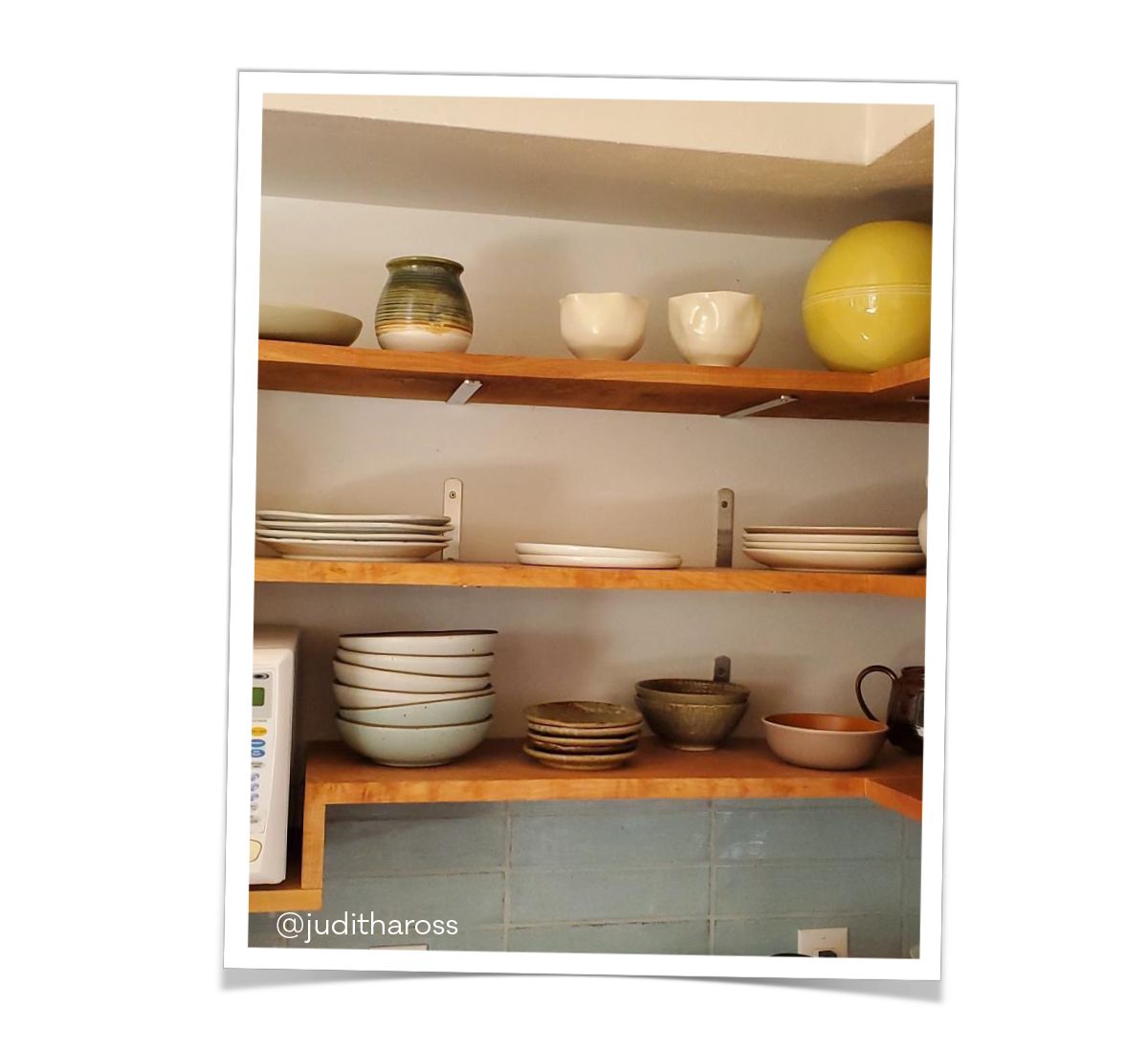 Floating wood shelves in a kitchen that hold ceramic plates, bowls, and cups.