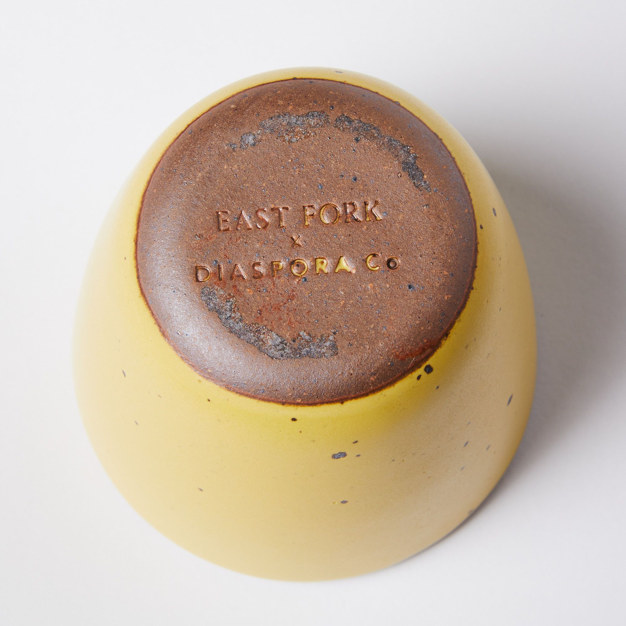 unglazed brown bottom of cylindrical yellow cup with East Fork x Diaspora stamp