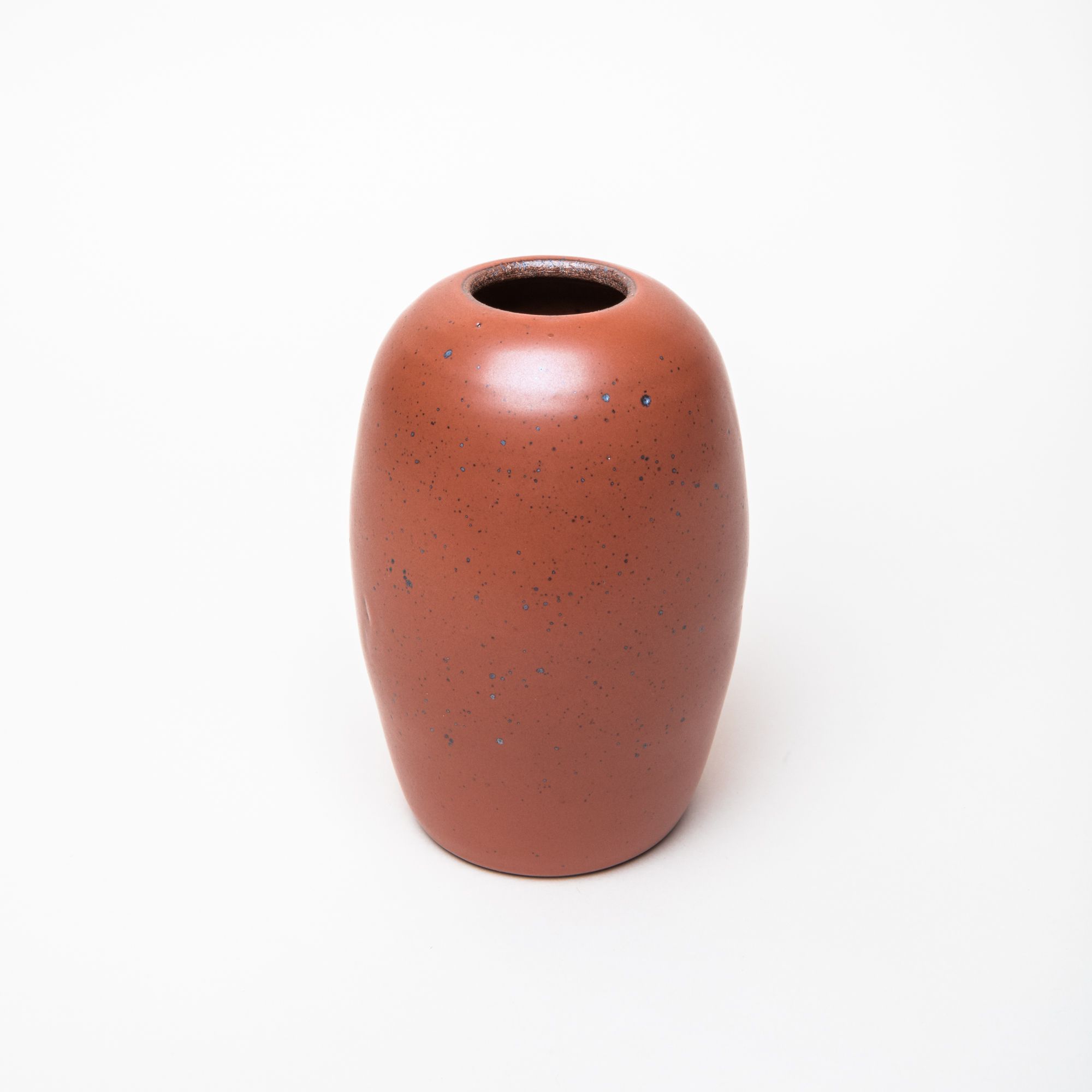 A ceramic vase in a cool burnt terracotta color featuring iron speckles with a long oval body and small opening on top