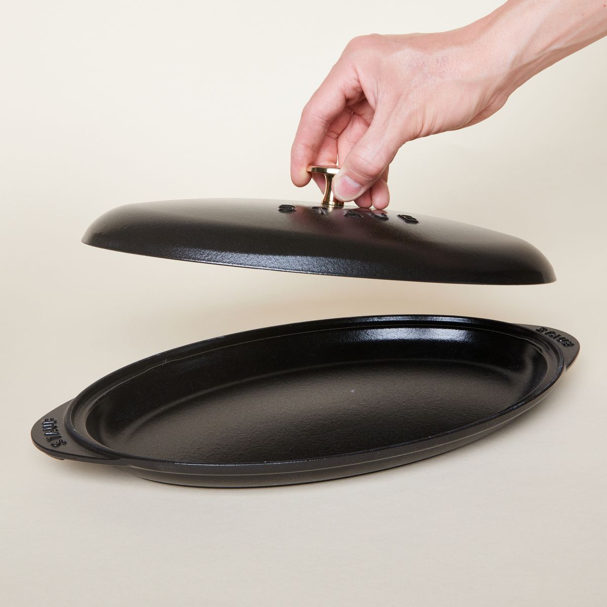 black oval platter with hand holding lid and gold handle 