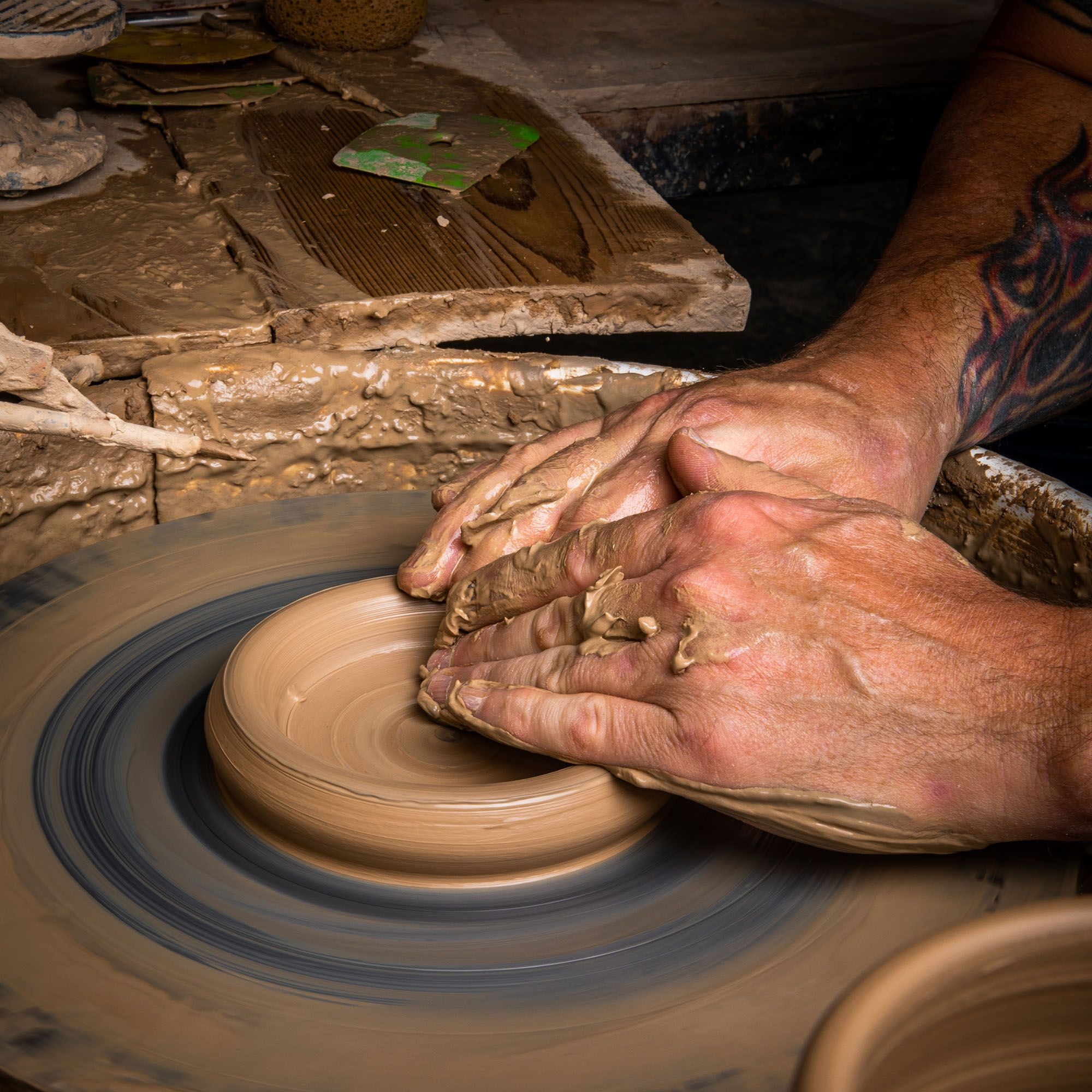 A person's hands form a piece of clay on the pottery wheel