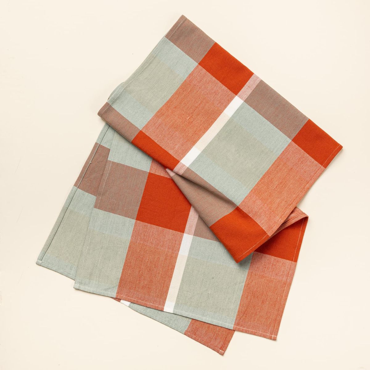 A gingham table runner featuring colors of sage green, bold orange, and cream.