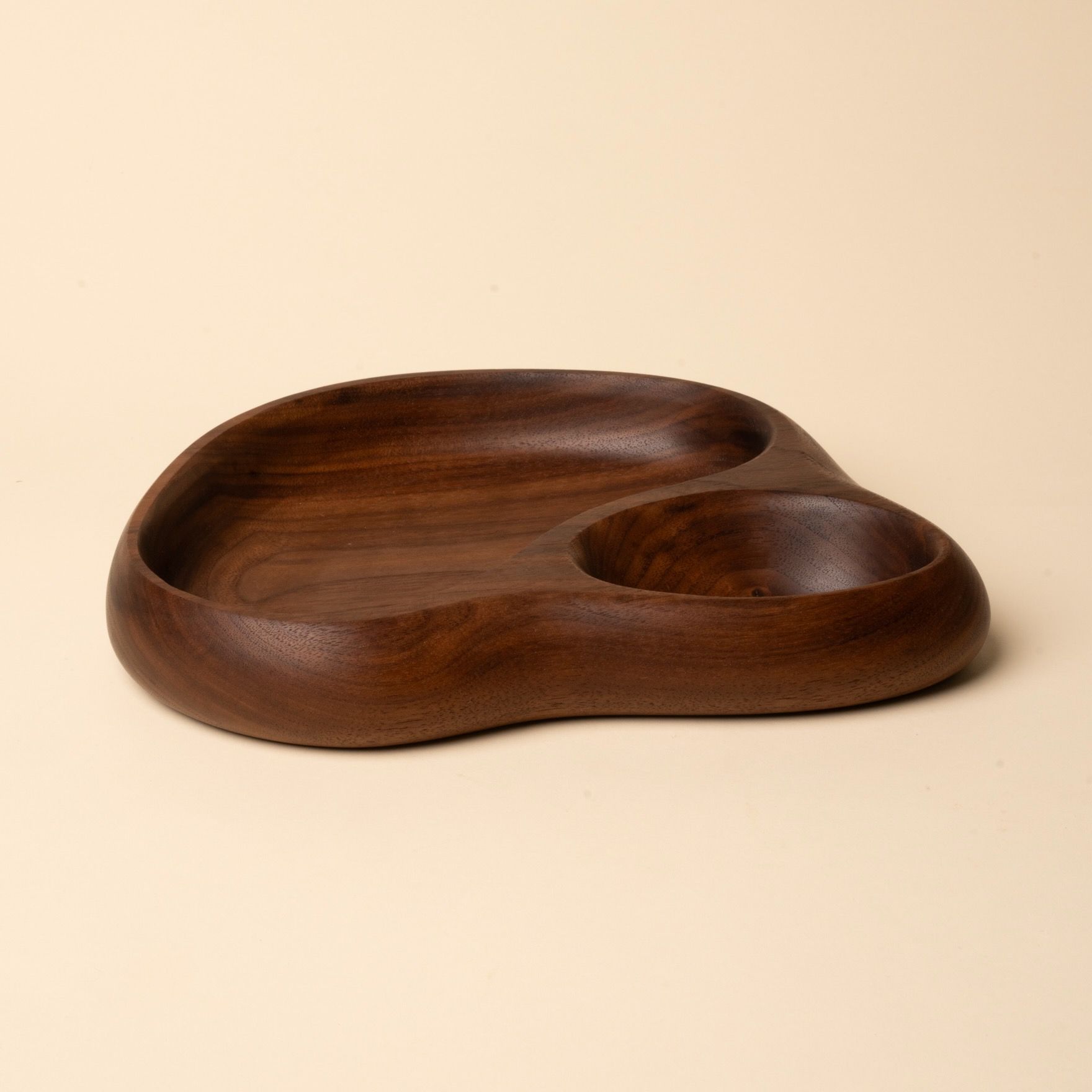 Carved walnut tray with smooth organic form, featuring two rounded compartments on a neutral backdrop.