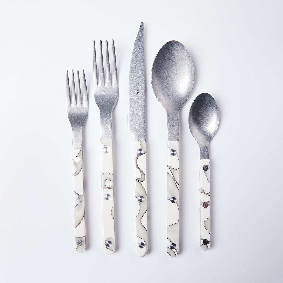 A group of silver, white and gray cutlery (salad fork, dinner fork, knife, soup spoon and teaspoon)