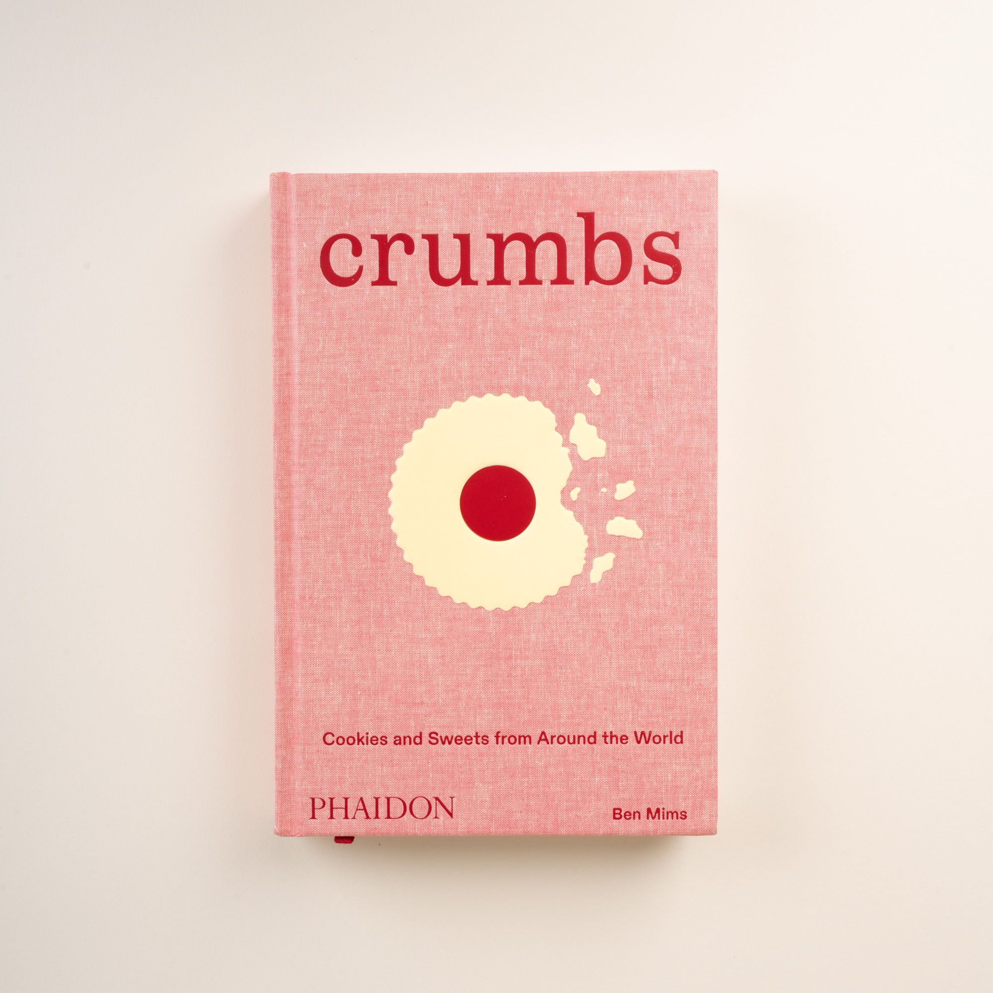 Front cover of 'Crumbs: Cookies and Sweets from Around the World' by Ben Mims, pink with cookie illustration.