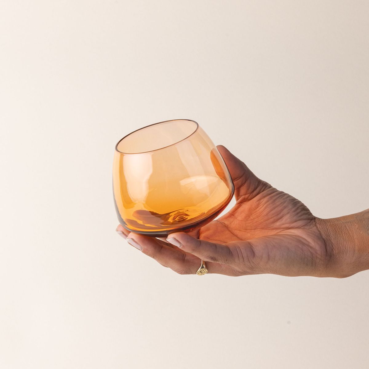 A hand holds a light orange glass whiskey snifter with a rounded base