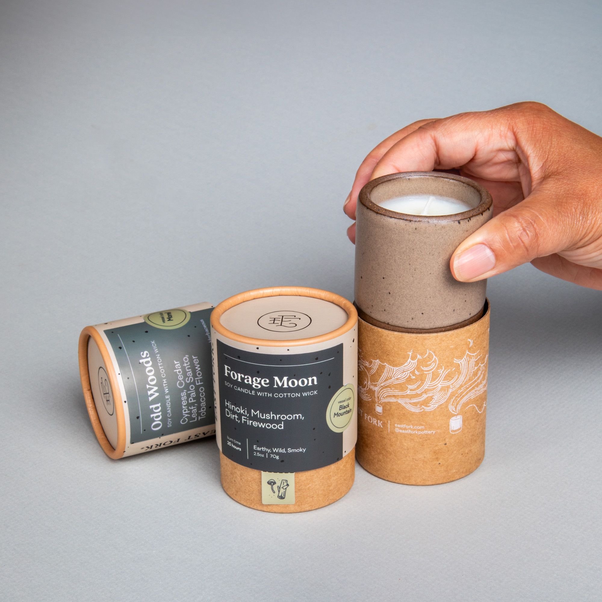 Two small cardboard packaging tubes with a candle inside each with branding on the outside that says 'Odd Woods' and 'Forage Moon'