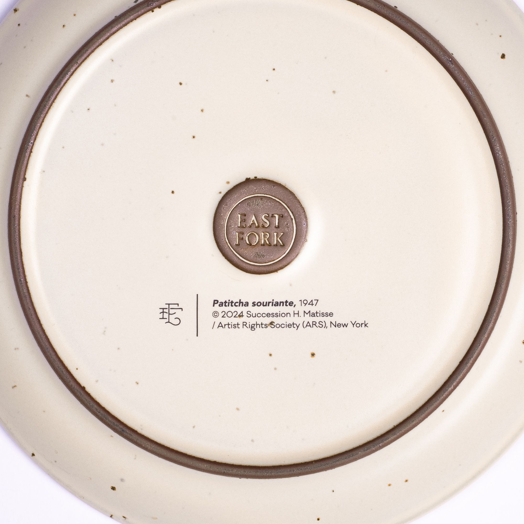The back of a side plate with an East Fork stamp with a small decal of information about the artwork, Patitcha souriante, by Henri Matisse.