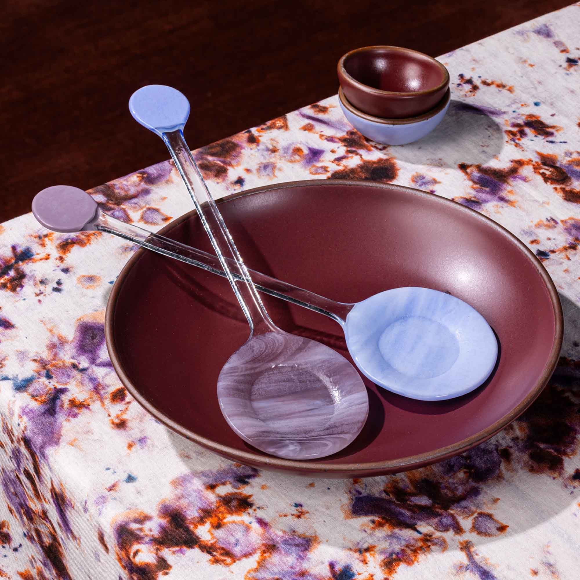 2 modern glass colorblocked serving spoons sit on a plum serving dish on a table