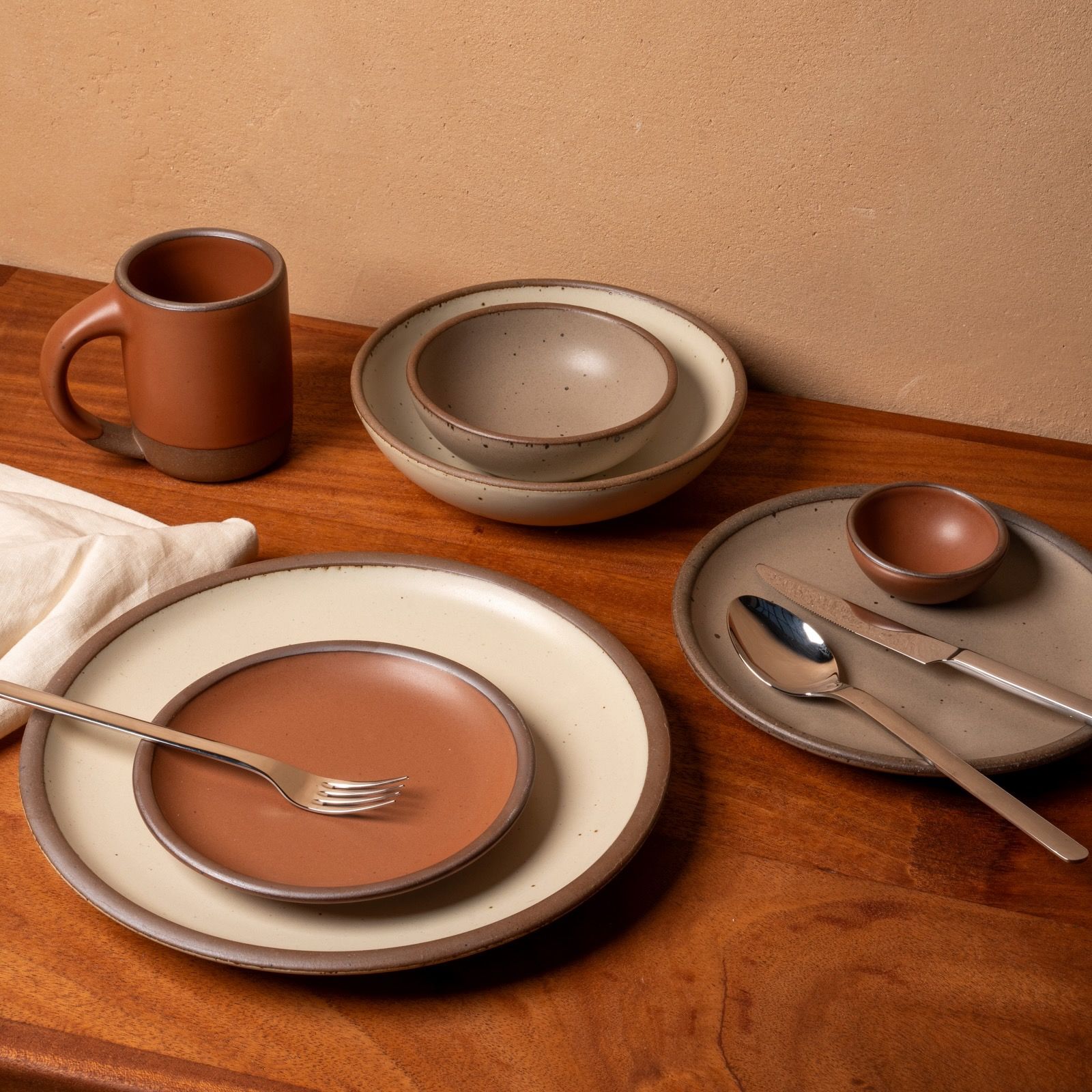 7 Piece You're All Set Set sitting on a table with silverware and a white linen napkin with colors including cool terracotta, warm pale brown, and warm off-white.