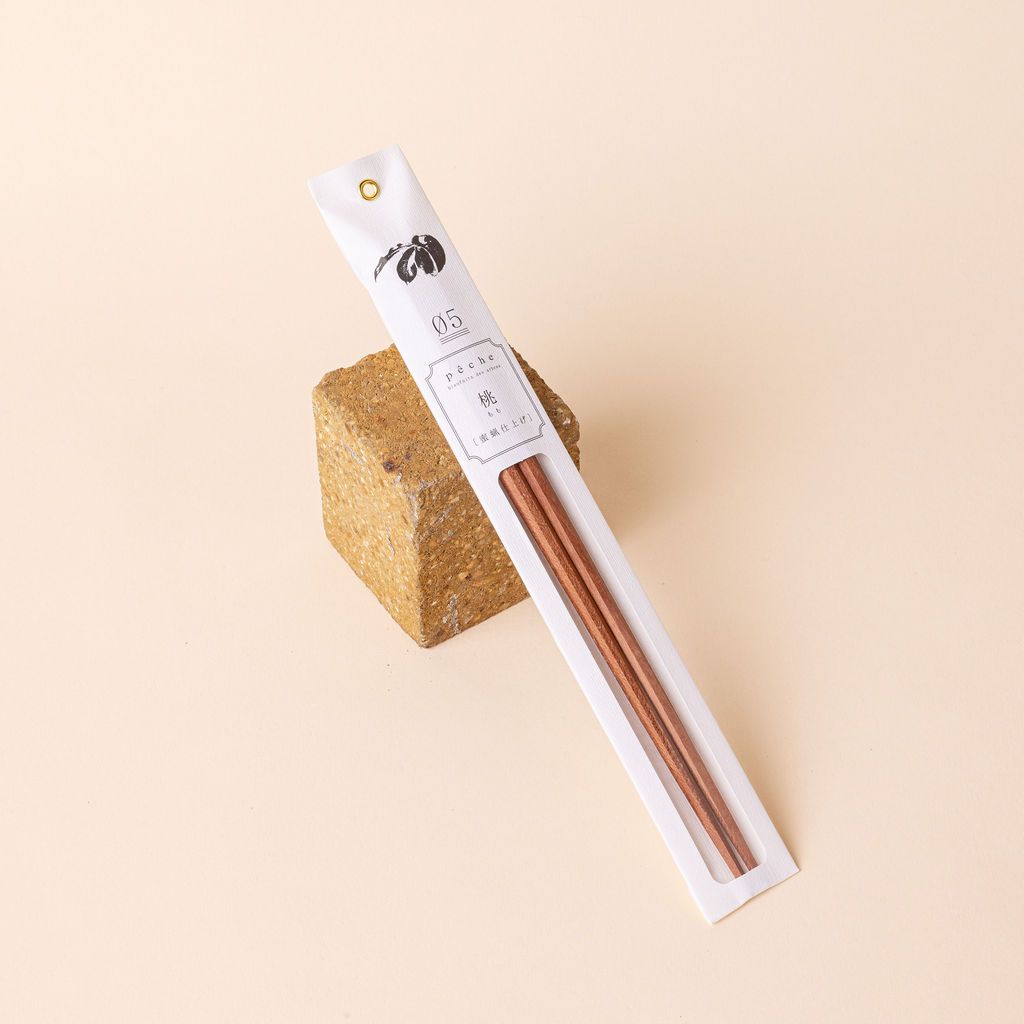 Simple pair of light brown wood chopsticks packaged in thin paper packaging leaning against a square brick