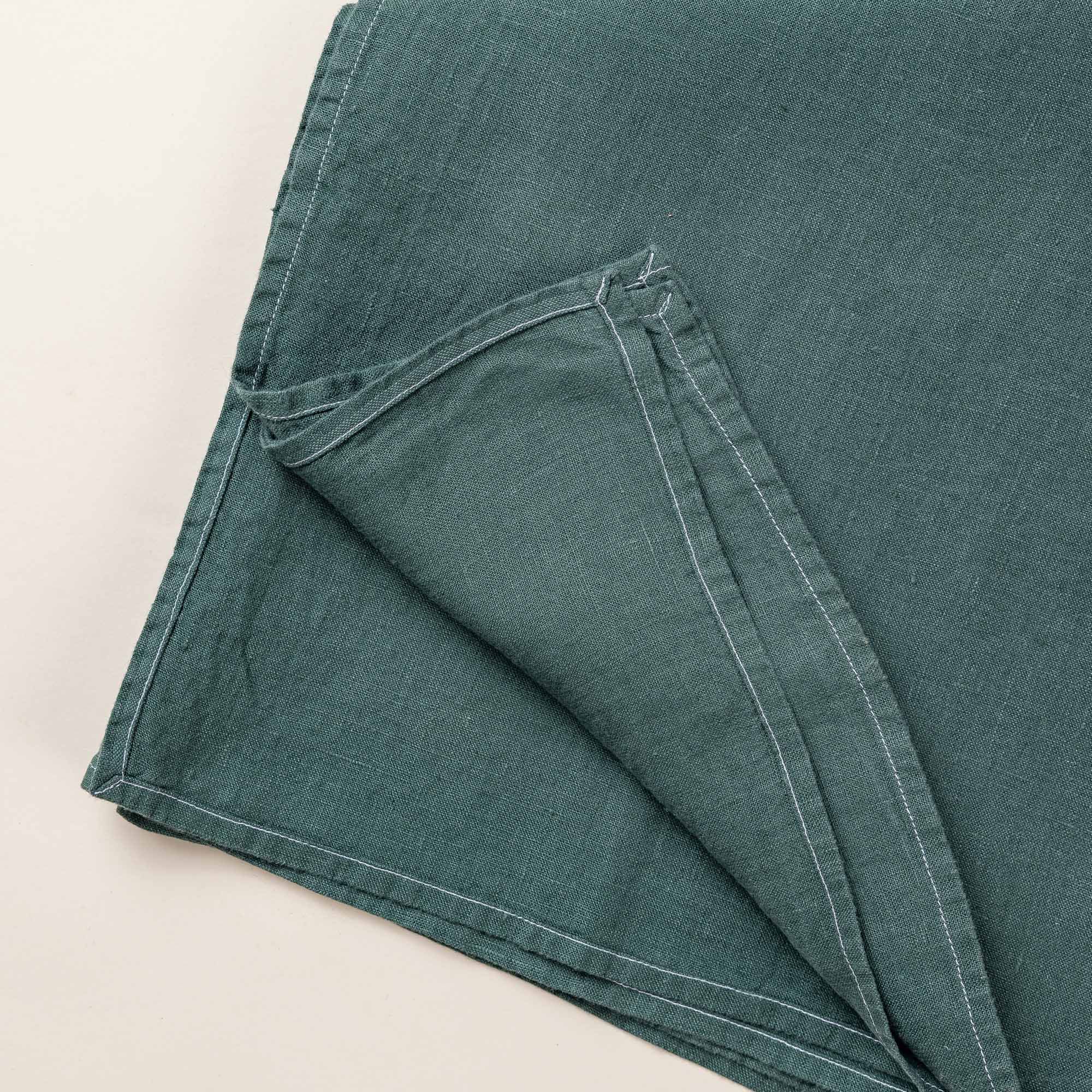 A closeup of the corner edge of a folded linen tablecloth in a solid deep teal color
