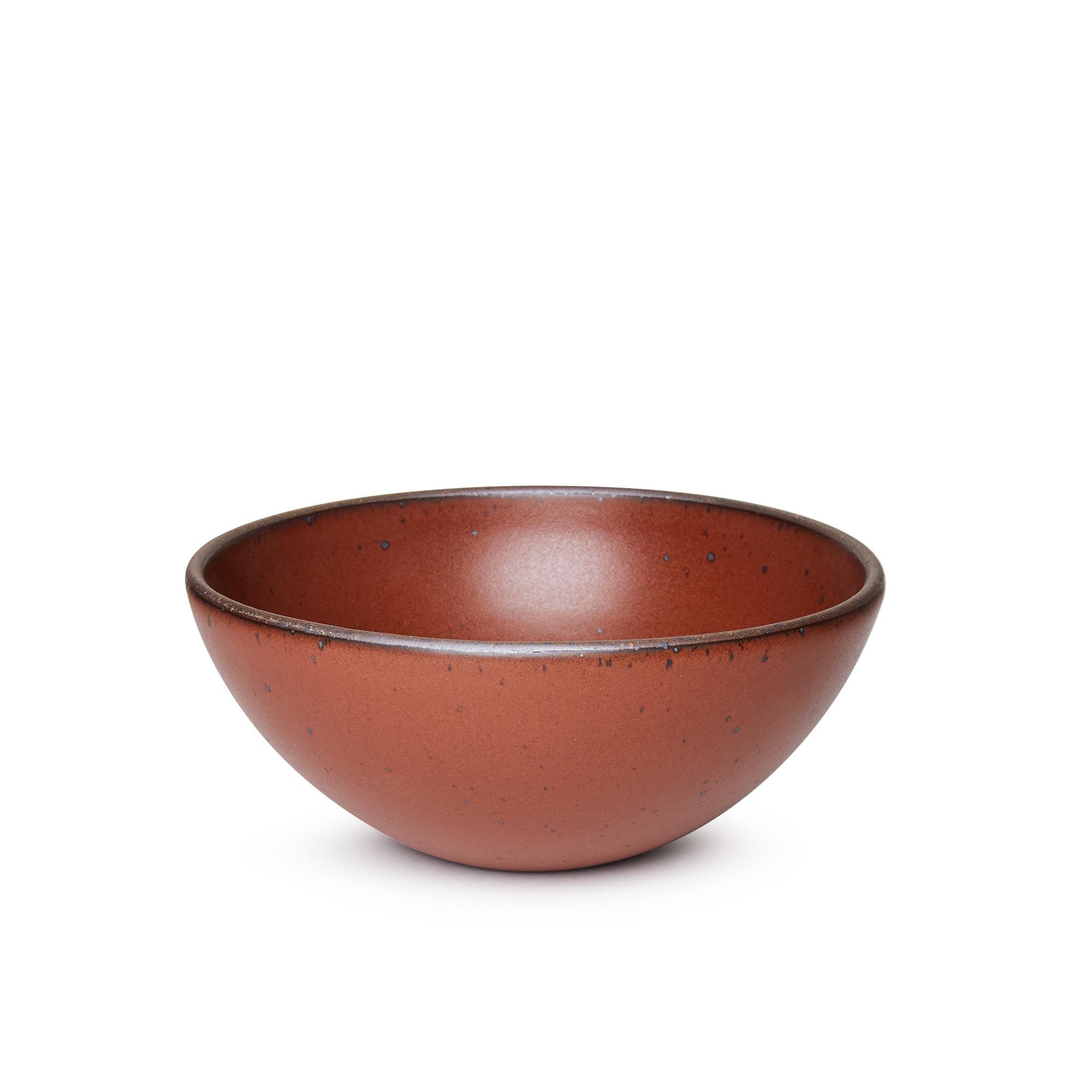 A large rounded ceramic bowl in a cool burnt terracotta color featuring iron speckles and an unglazed rim